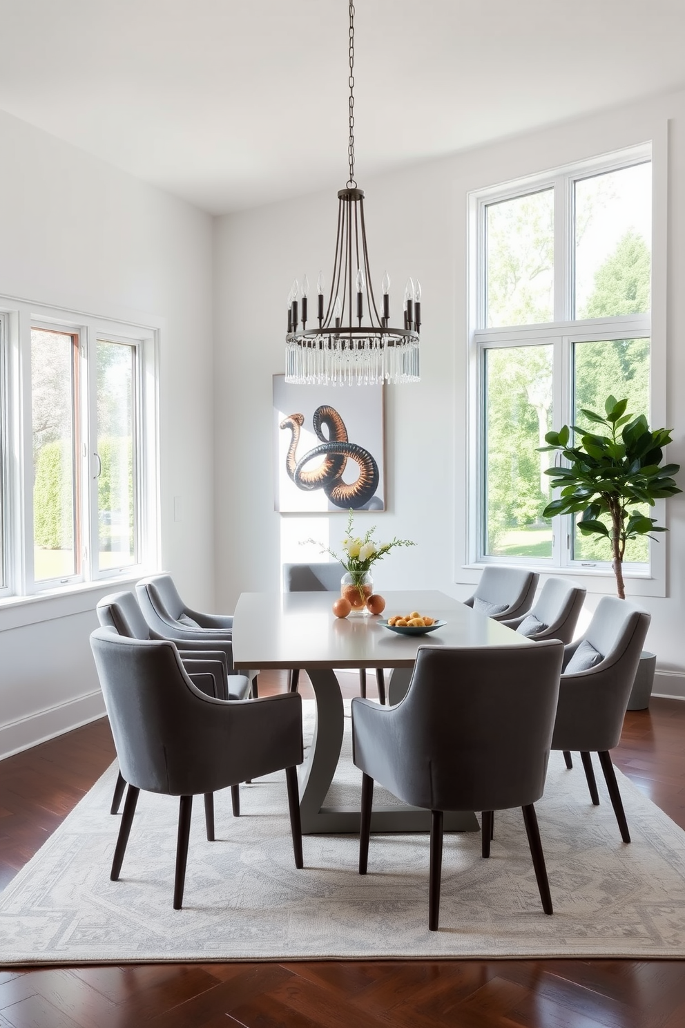 A modern dining room featuring gray dining chairs with plush upholstery arranged around a sleek rectangular table. The walls are painted in a soft white hue, and large windows allow natural light to fill the space, enhancing the cozy atmosphere. A statement chandelier hangs above the table, adding elegance to the room. The floor is covered with a light-colored area rug that complements the gray tones of the chairs, creating a harmonious and inviting dining environment.