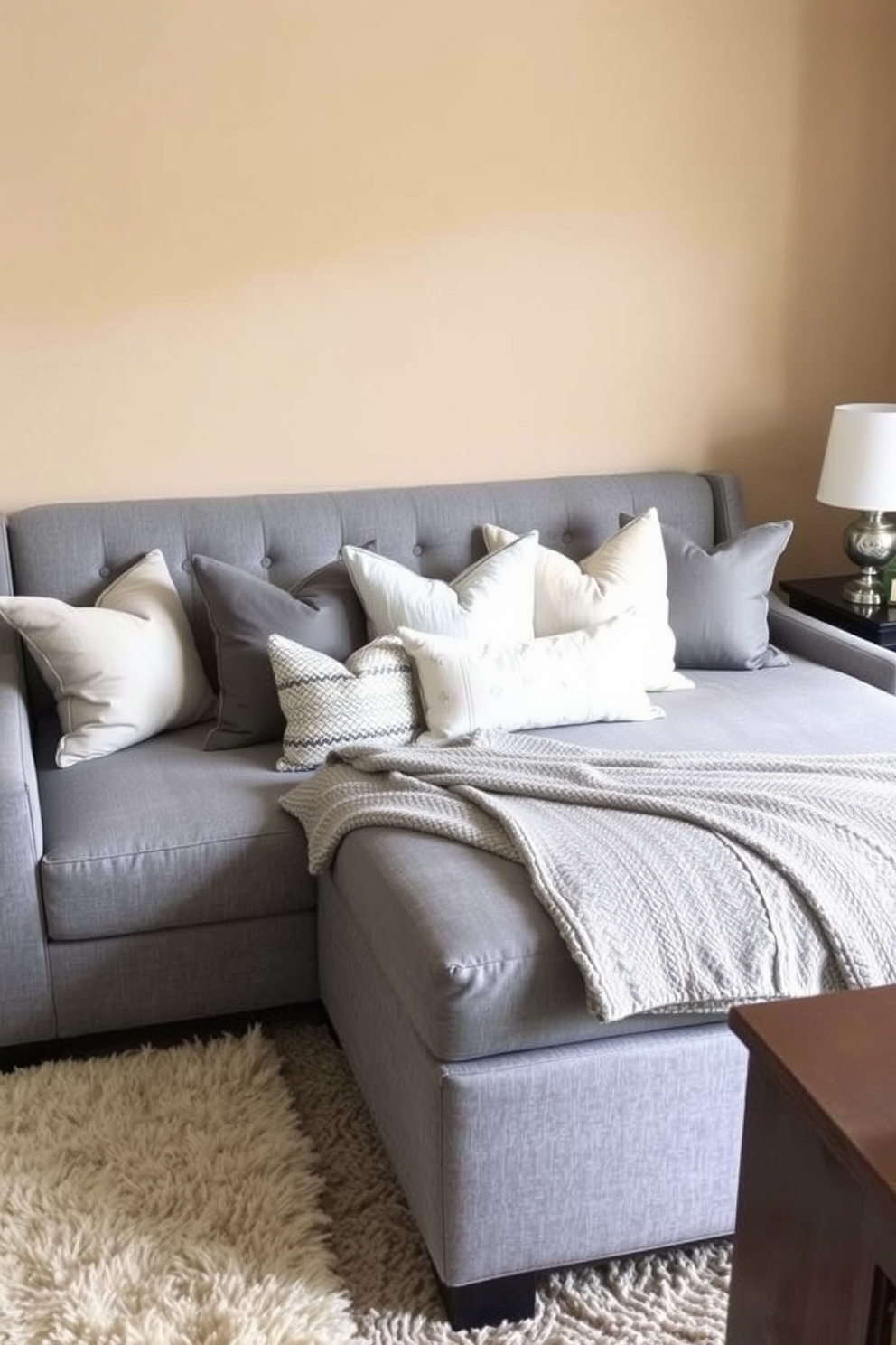 A cozy family room features a gray upholstered bed that doubles as a stylish seating area. Soft throw pillows in various shades of gray and cream are arranged on the bed for added comfort. The walls are painted in a warm, neutral tone that complements the gray upholstery. A plush area rug anchors the space, while a few decorative items on the bedside tables add a personal touch.