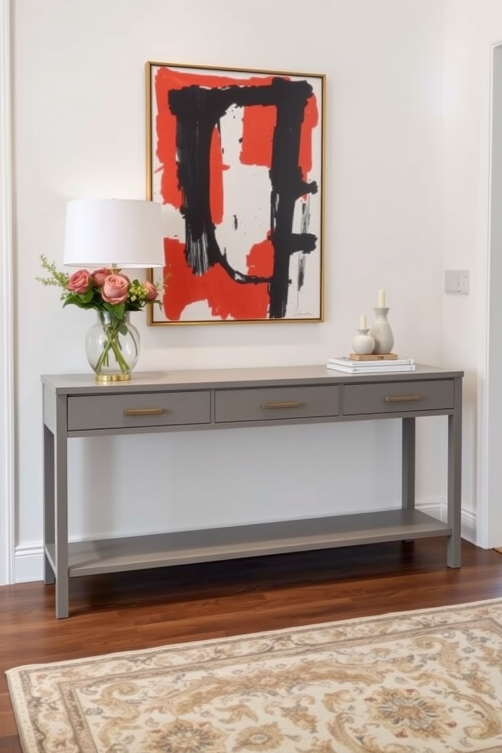 Elegant gray console table with artwork display. The table is adorned with a striking piece of modern art that adds a pop of color to the space. The foyer features soft lighting that highlights the console's sleek lines. A stylish rug in neutral tones anchors the entryway, creating a warm and inviting atmosphere.