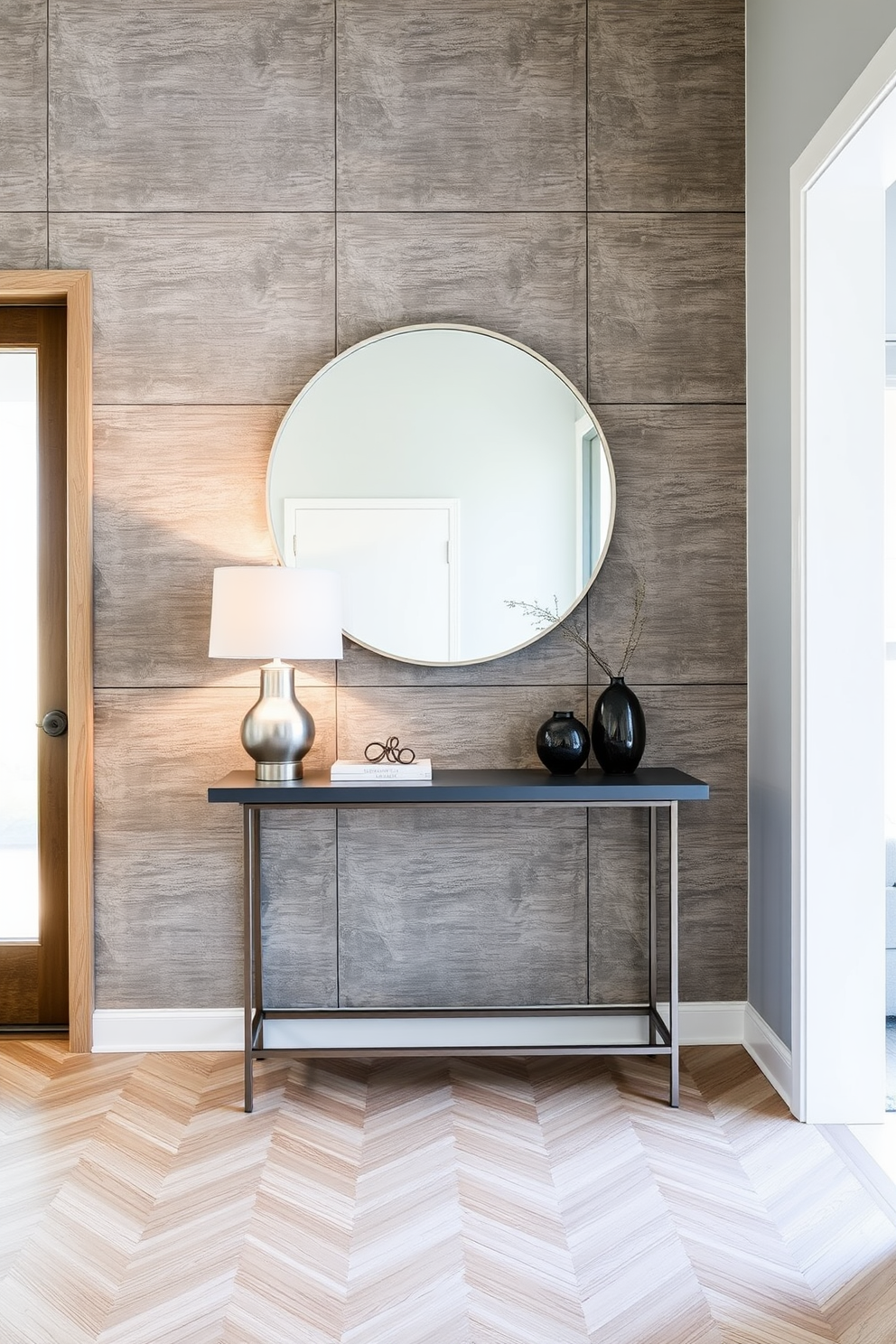 Textured gray wall panels create a striking backdrop in the foyer, adding depth and sophistication to the space. A sleek console table with a minimalist design sits against the wall, adorned with a modern lamp and decorative accents. The flooring features a subtle herringbone pattern in light wood, complementing the gray tones of the walls. A large round mirror hangs above the console table, reflecting natural light and enhancing the airy feel of the foyer.