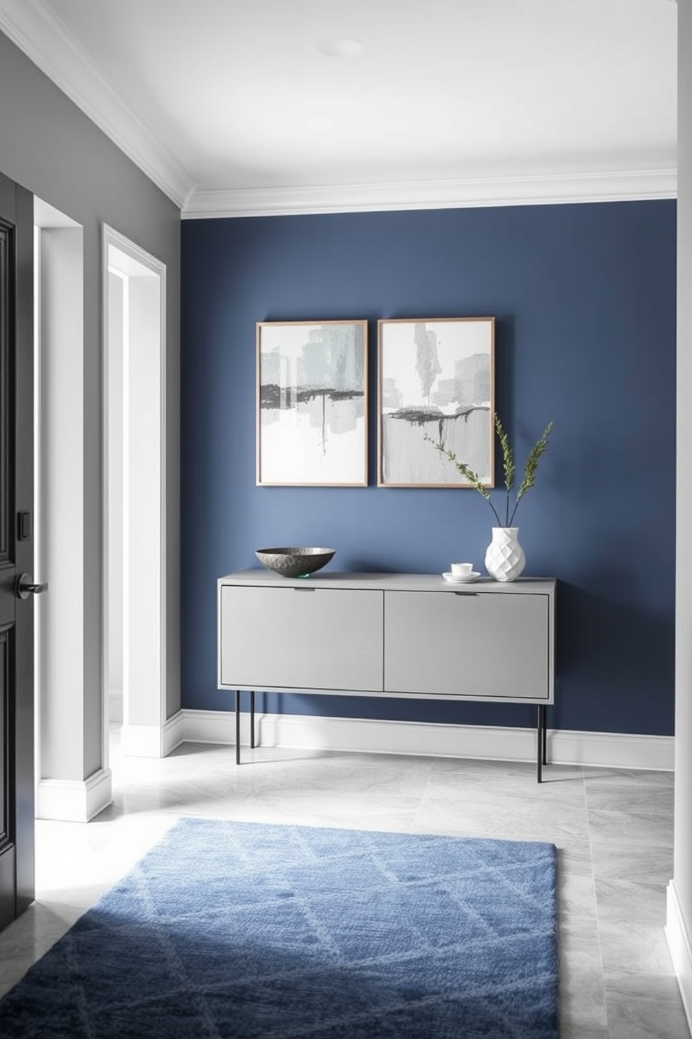 A serene foyer designed with a gray and blue color palette that evokes a sense of calm. The walls are painted in a soft gray, complemented by a blue accent wall featuring abstract artwork. A sleek console table in a muted gray finish sits against the wall, adorned with a decorative bowl and a small potted plant. The flooring consists of light gray tiles, and a cozy blue area rug adds warmth underfoot.