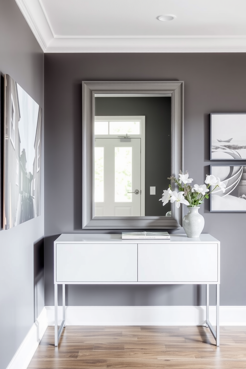 A stylish entryway featuring a gray color palette. The walls are adorned with contemporary gray artwork that enhances the overall decor. The foyer includes a sleek console table with a minimalist design. A large mirror with a gray frame hangs above the table, reflecting natural light and adding depth to the space.