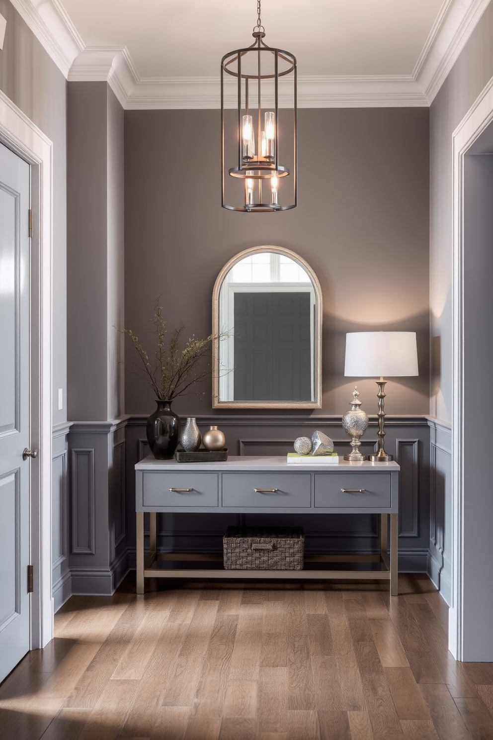 A stylish foyer featuring gray wainscoting that adds depth and elegance to the space. The contrasting trim accents highlight the architectural details and create a sophisticated atmosphere. A large console table sits against the wall, adorned with decorative items and a statement mirror above it. Soft lighting from a modern chandelier casts a warm glow, enhancing the inviting ambiance of the gray foyer.