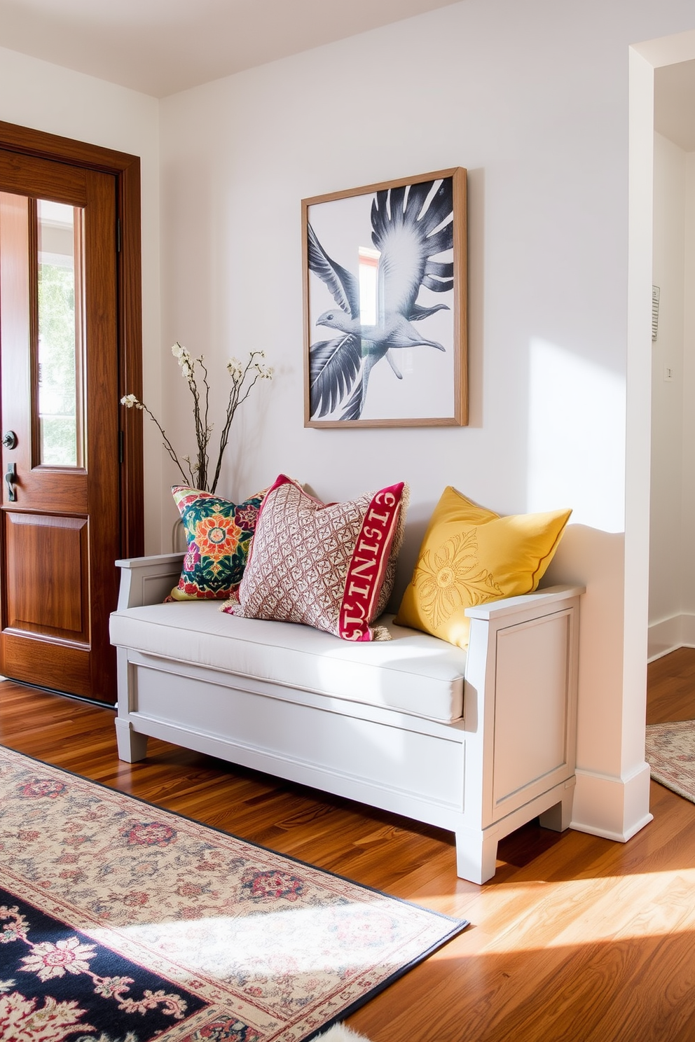 A soft gray bench is positioned against the wall in the foyer, adorned with an array of colorful throw pillows that add a vibrant touch. The flooring features elegant hardwood, complemented by a stylish area rug that enhances the welcoming atmosphere.