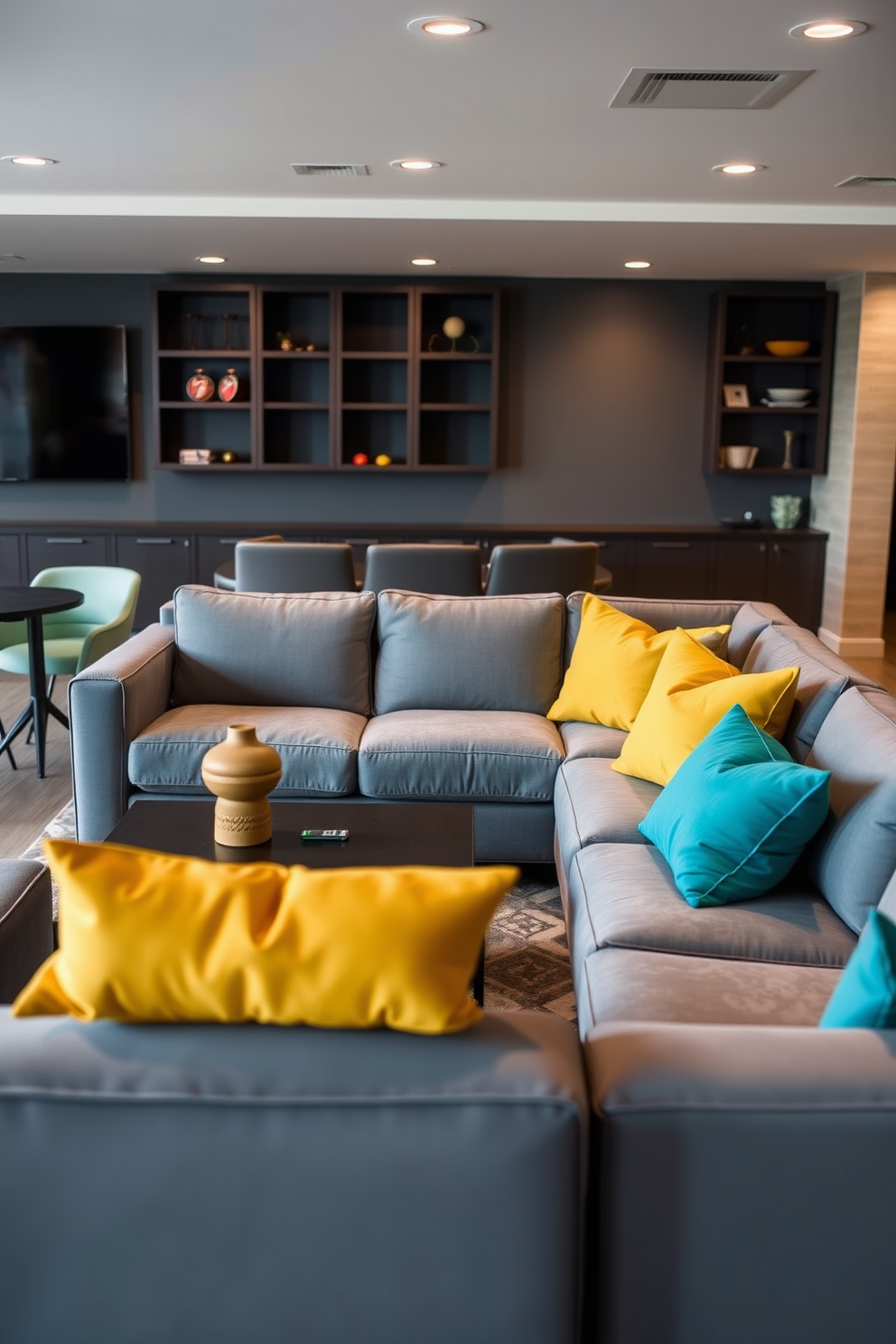 Sleek gray furniture is arranged in a modern game room, featuring a plush sectional sofa and a stylish coffee table. Vibrant cushions in shades of teal and mustard add a pop of color, creating a lively and inviting atmosphere.