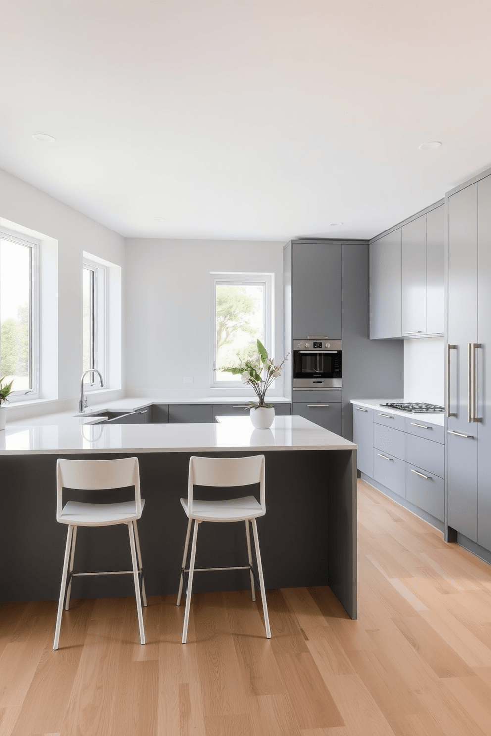 A minimalist gray kitchen featuring sleek lines and a streamlined design. The cabinetry is a soft gray with handleless doors, complemented by a white quartz countertop and a subtle backsplash. A central island provides additional workspace and includes minimalist bar stools. The flooring is light wood, enhancing the airy feel of the space while large windows allow natural light to flood in.