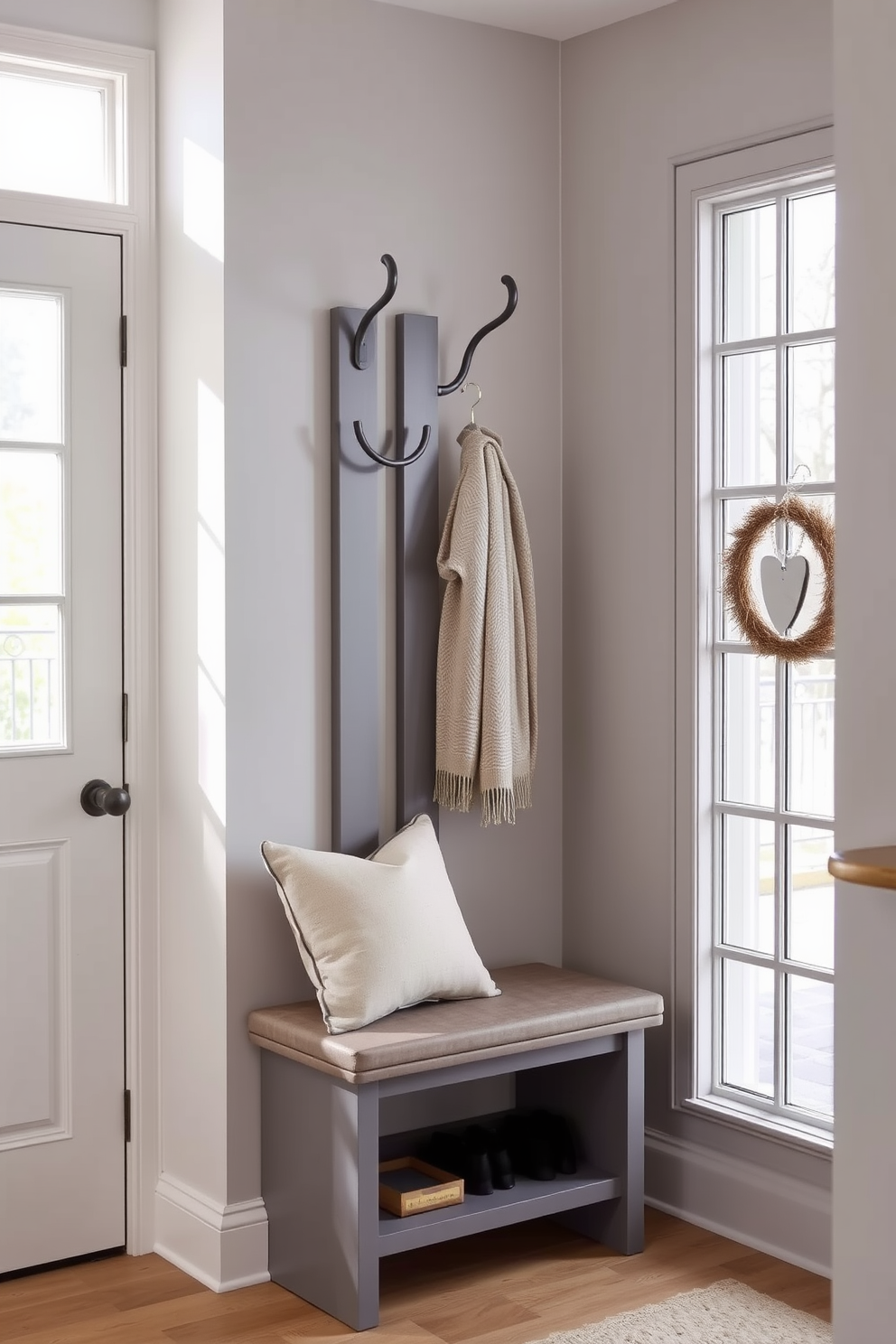 A stylish gray coat rack stands against the wall, featuring sleek lines and a modern design. Below the rack, a comfortable bench provides seating, adorned with plush cushions for added comfort. The mudroom is designed with a soft gray color palette, creating a welcoming atmosphere. Natural light floods the space through a nearby window, highlighting the elegant storage solutions and decorative accents.