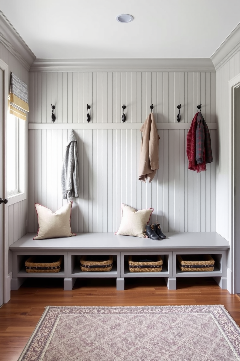 A gray mudroom featuring elegant beadboard paneling creates a classic and inviting atmosphere. The space includes built-in benches with plush cushions and hooks for hanging coats, complemented by a stylish area rug.