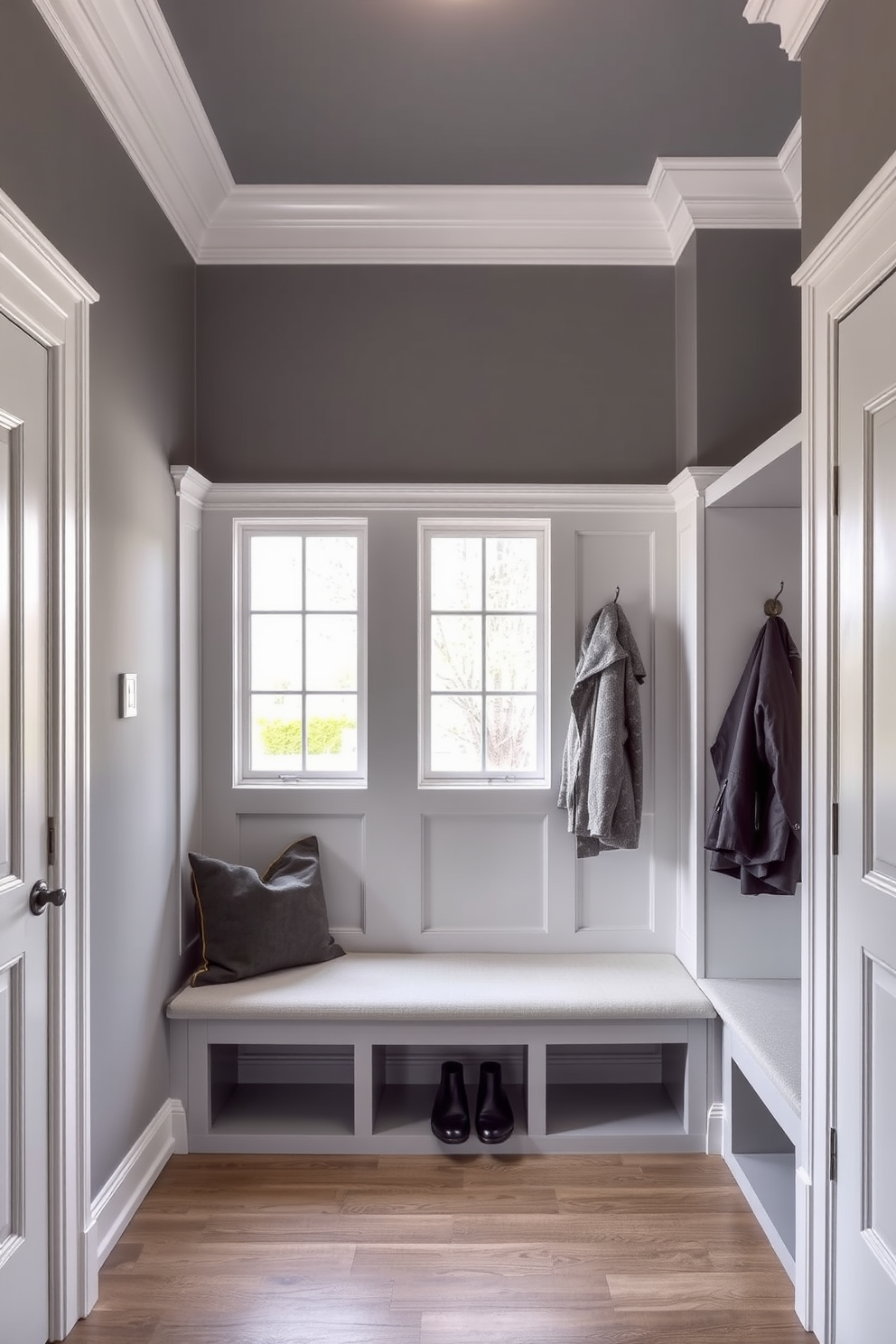 A sophisticated gray mudroom featuring elegant crown molding that adds a touch of refinement. The space includes built-in benches with plush cushions and stylish hooks for coats, creating a welcoming entryway.