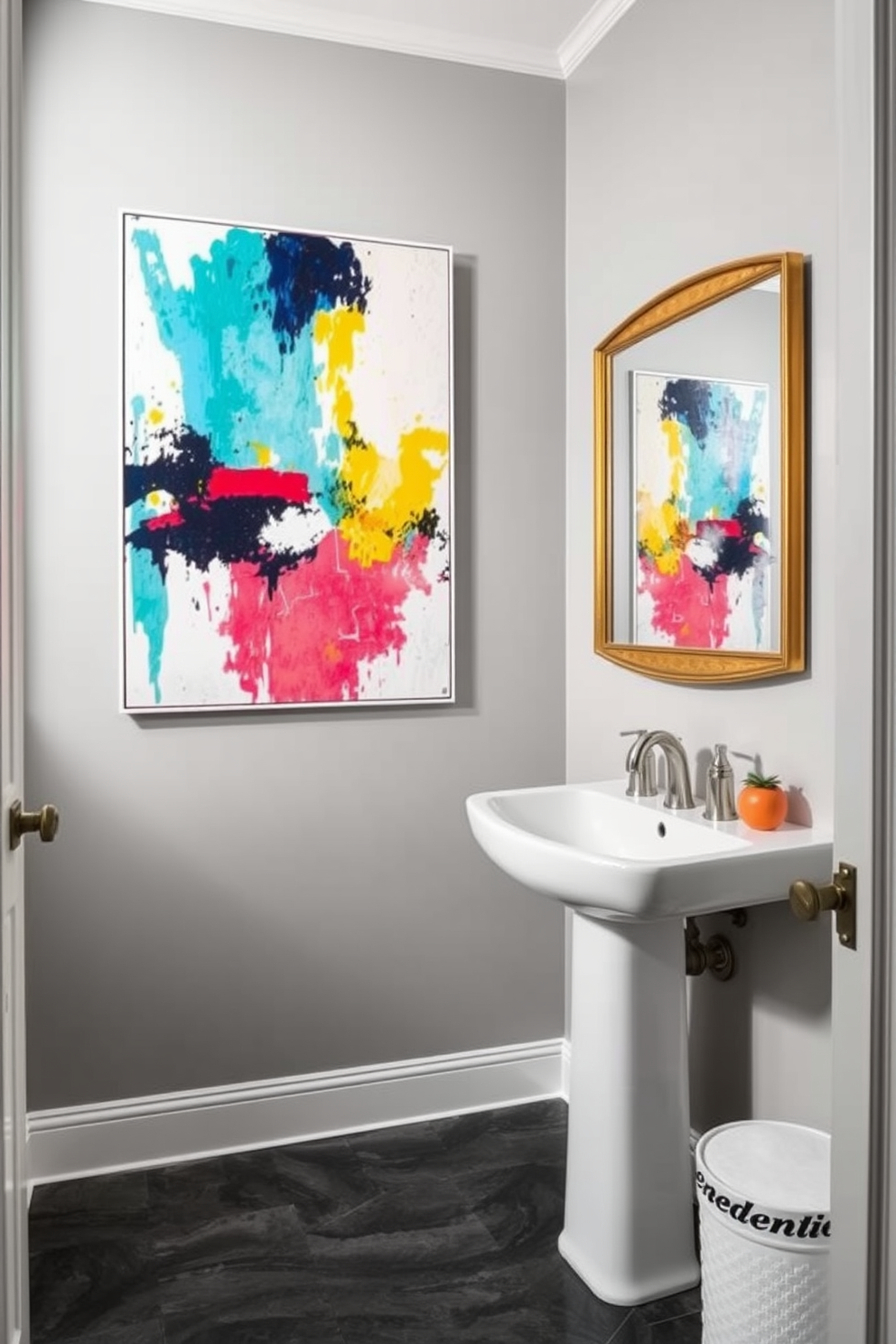 Bright artwork to contrast gray tones in a chic powder room. The walls are painted in a soft gray, and a sleek white pedestal sink is positioned against one wall. A large, colorful abstract painting hangs prominently above the sink, adding a vibrant focal point. The floor features dark gray tiles, while a stylish mirror with a gold frame reflects the artwork and enhances the space.