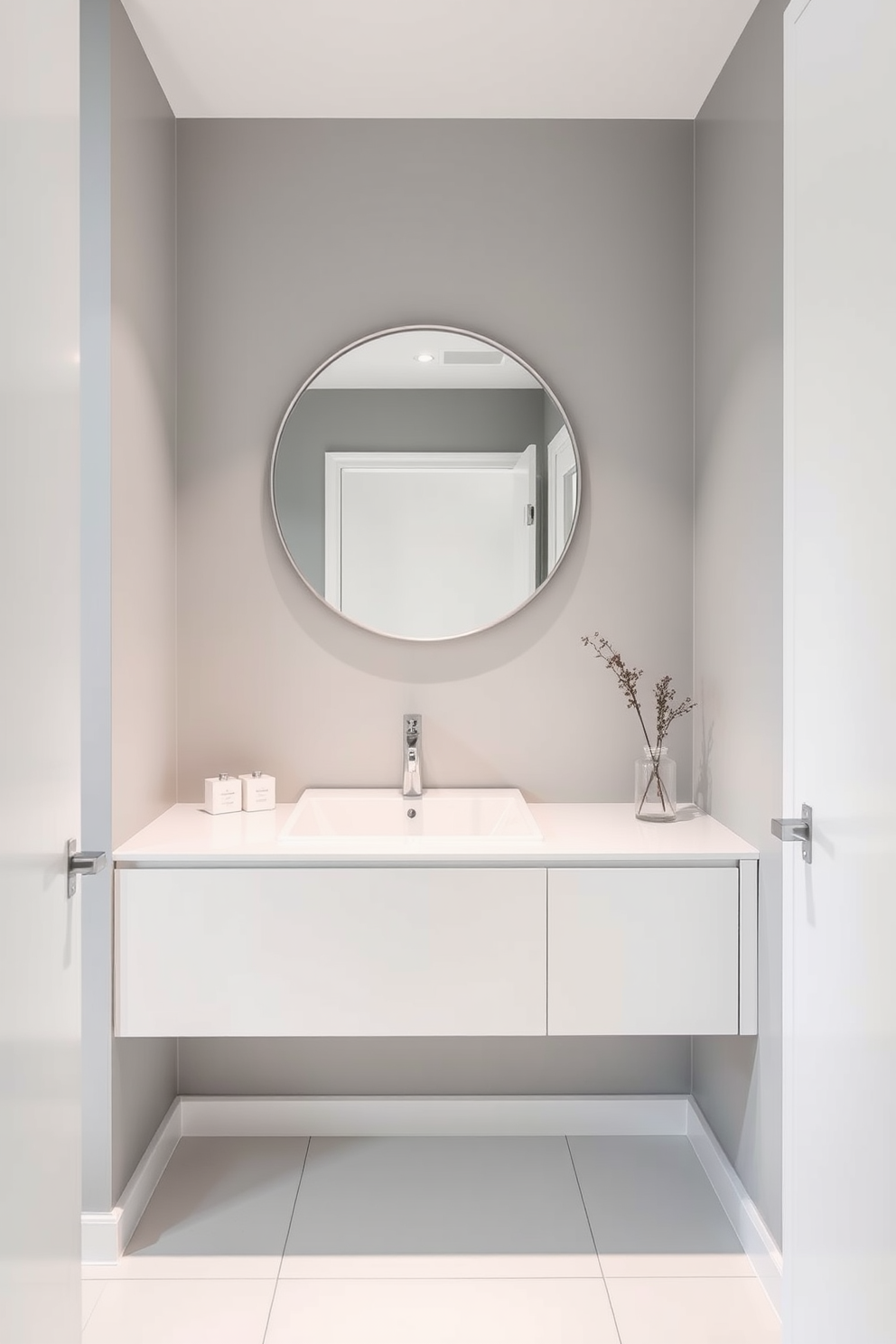 A minimalist powder room featuring a sleek gray and white color palette. The walls are painted in a soft gray, complemented by a white floating vanity with a simple rectangular sink. A large round mirror with a thin frame hangs above the vanity, reflecting the clean lines of the space. The floor is covered in large white tiles, creating a spacious and airy feel.