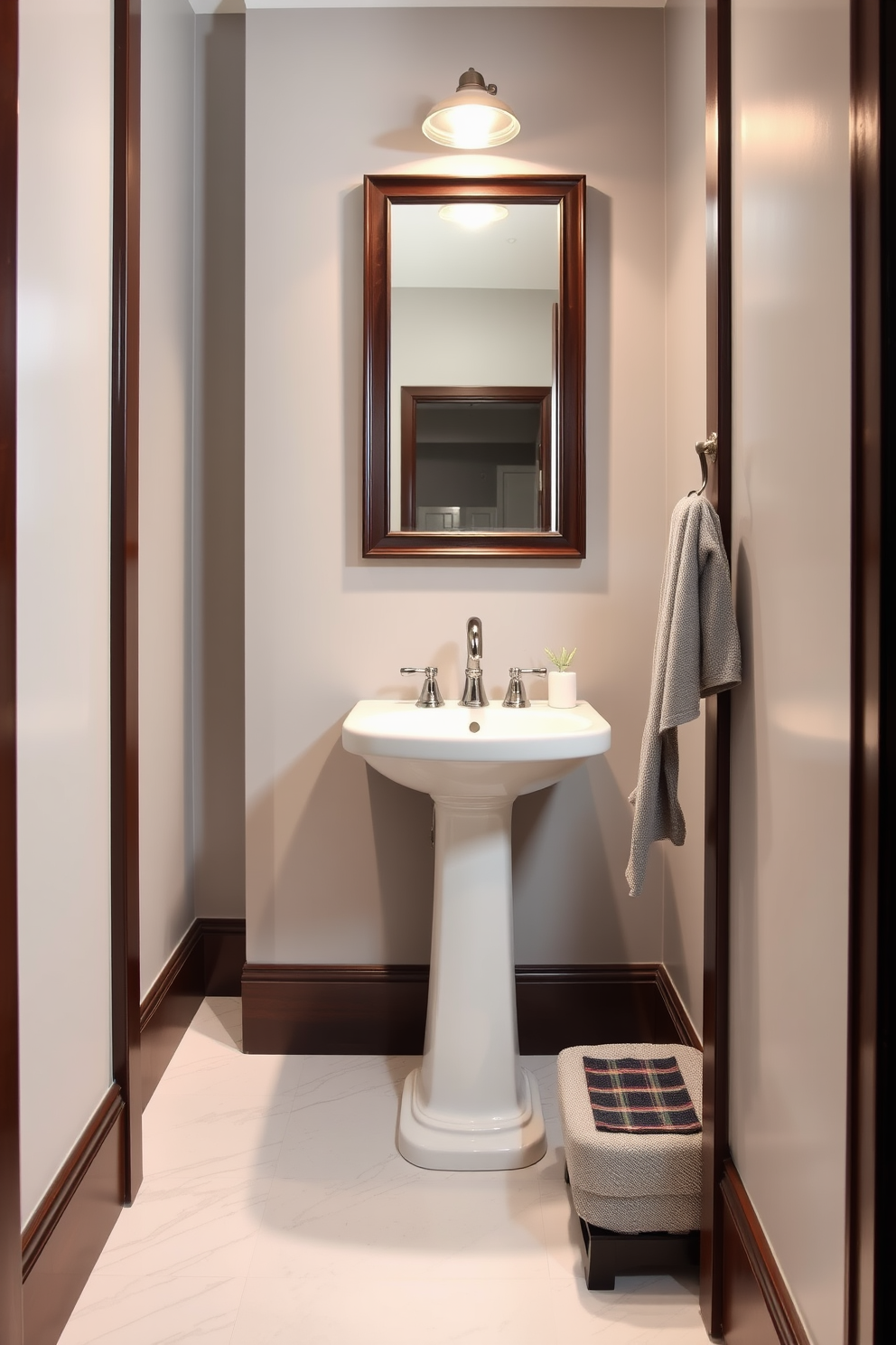 A chic powder room featuring light gray walls complemented by rich dark wood trim. The space includes a sleek pedestal sink with a stylish mirror above, framed in dark wood to match the trim. The floor is adorned with elegant white marble tiles that contrast beautifully with the gray paint. A small wooden cabinet provides storage, and a plush gray towel is neatly hung on a hook nearby.