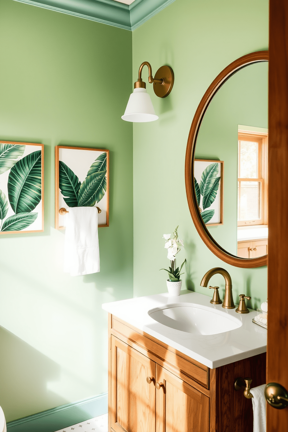 A serene green bathroom adorned with tropical leaf prints in the artwork. The walls are painted in a soft mint green, complementing the vibrant colors of the leaf prints. Elegant fixtures in brushed gold add a touch of luxury to the space. A wooden vanity with a white countertop is paired with a large round mirror, enhancing the tropical theme.