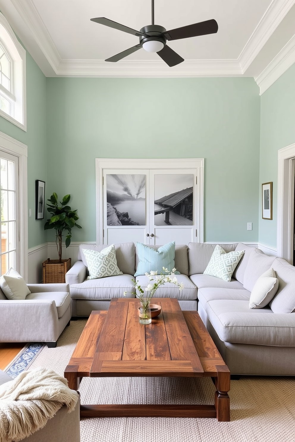 Soft mint green walls provide a calming backdrop for a cozy family room. The white trim adds a crisp contrast, enhancing the room's brightness and inviting atmosphere. A plush sectional sofa in light gray is centered around a rustic wooden coffee table. Complementing the seating, a soft area rug in neutral tones anchors the space and adds warmth.