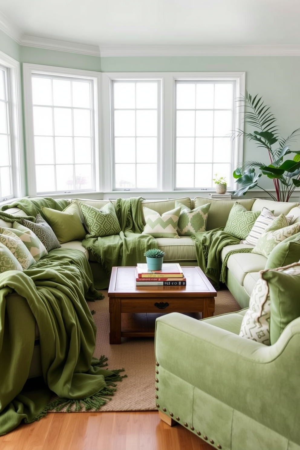 A cozy green living room filled with soft green throws draped over a plush sectional sofa. The walls are painted in a light mint shade, and large windows allow natural light to flood the space. Accent pillows in various shades of green and patterned textiles add depth to the seating area. A wooden coffee table sits in the center, adorned with a stack of books and a small potted plant for a touch of nature.