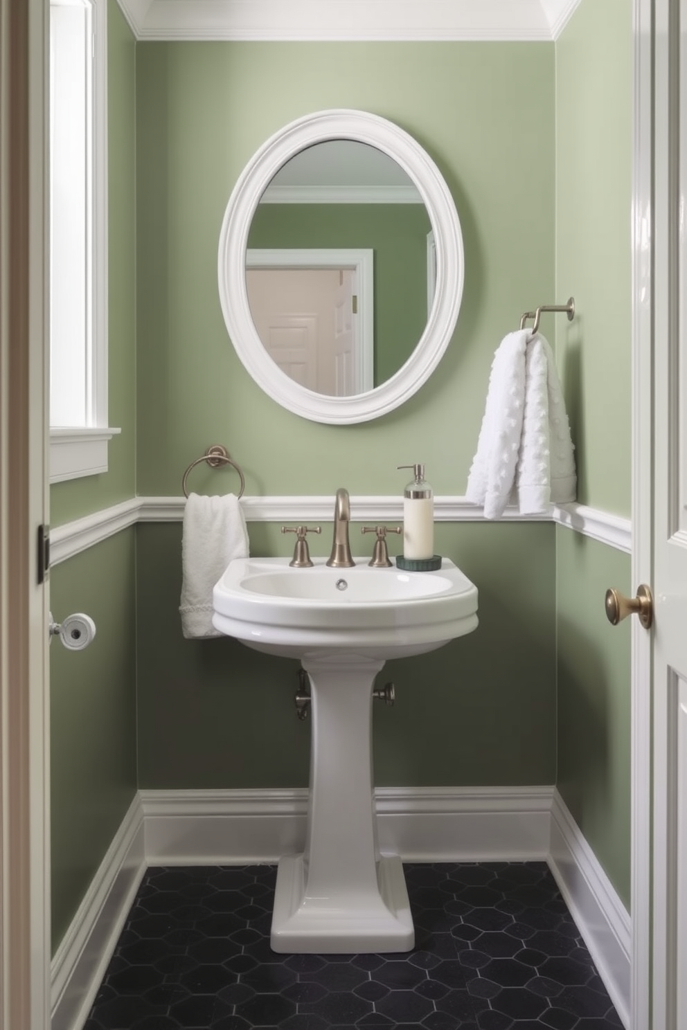 A chic powder room featuring sage green walls complemented by crisp white trim. The space includes a stylish pedestal sink with a brushed nickel faucet and a round mirror above it, reflecting the elegant decor. A plush white towel neatly hung on a decorative rack adds a touch of luxury. The floor is adorned with small hexagonal tiles in a contrasting dark shade, enhancing the room's sophisticated ambiance.