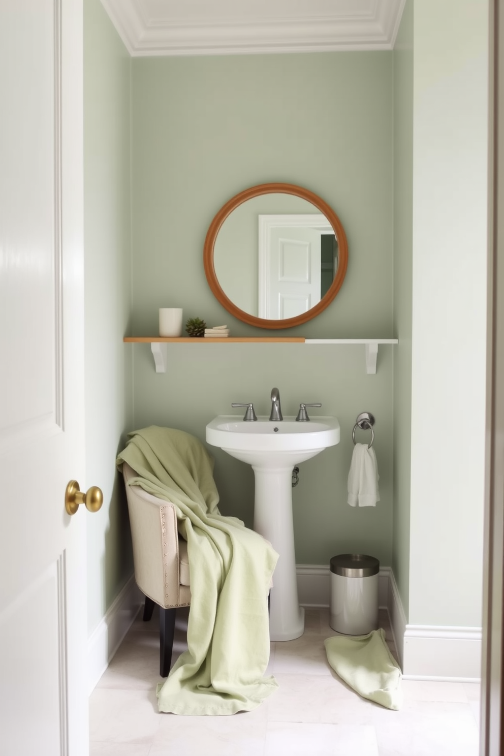 A serene powder room featuring soft green linens draped elegantly over a plush armchair. The decor is minimalistic with neutral tones, including a simple wooden shelf adorned with a few tasteful accessories. The walls are painted in a soft mint green, creating a calming atmosphere. A sleek white pedestal sink complements the overall design, with a round mirror framed in natural wood above it.