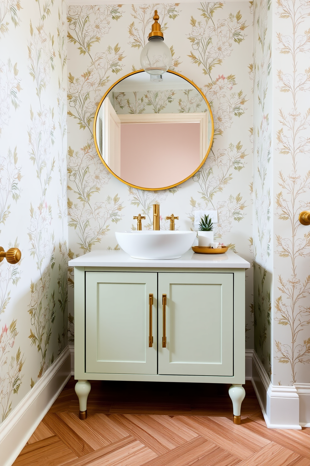 A pale mint vanity with brass hardware sits against the wall, complemented by a stylish white vessel sink. The walls are adorned with elegant floral wallpaper, creating a fresh and inviting atmosphere in the powder room. A round mirror with a brass frame hangs above the vanity, reflecting the soft glow of a vintage-style light fixture. The floor features a chic herringbone pattern in light wood, adding warmth and sophistication to the space.