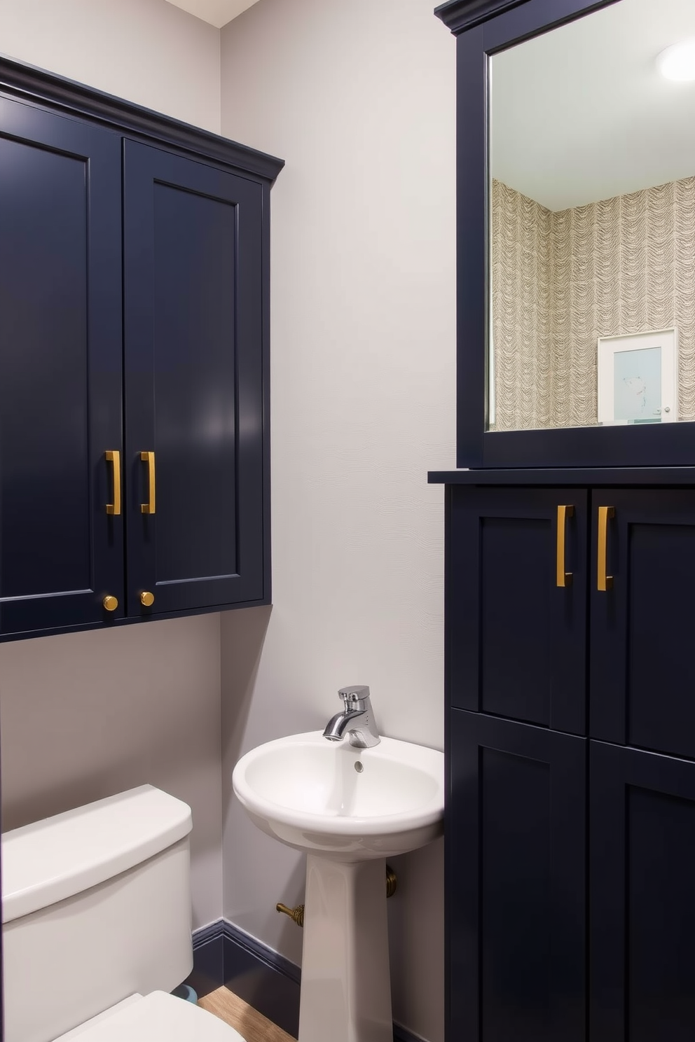 A stylish half bath featuring custom cabinetry designed for personalized storage. The cabinetry is finished in a rich navy blue with brass hardware, providing both functionality and elegance. The space includes a sleek pedestal sink complemented by a wall-mounted mirror with integrated lighting. Soft gray walls and a textured wallpaper accent create a warm and inviting atmosphere.