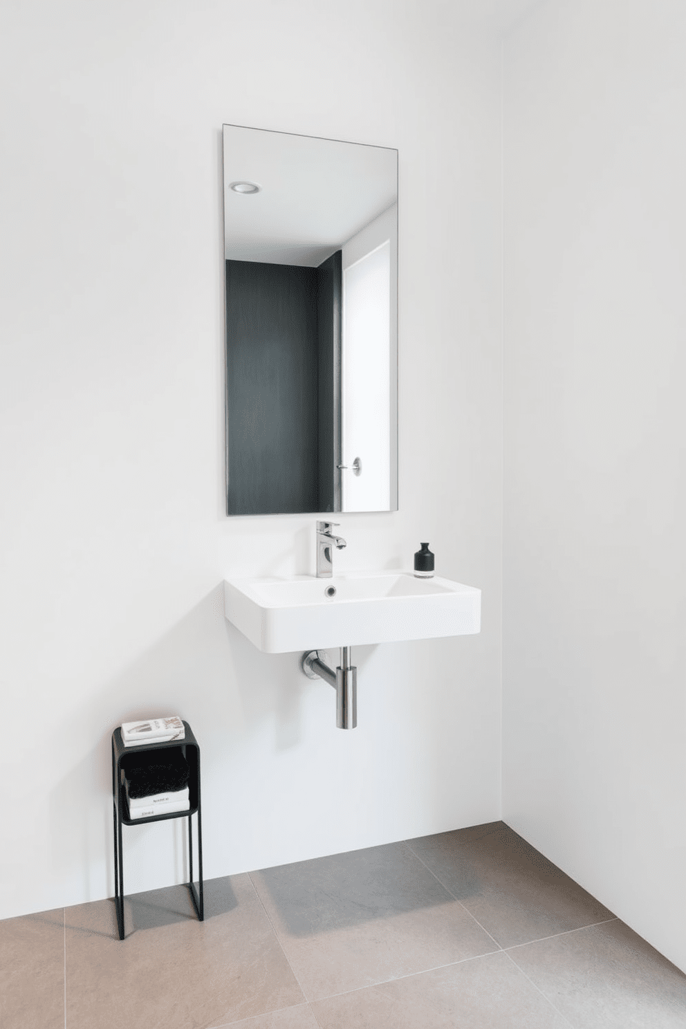 A floating sink is mounted on a sleek wall, showcasing a minimalist design that emphasizes modern elegance. The surrounding walls are painted in a crisp white hue, complemented by a stylish mirror that adds depth and sophistication to the space. The flooring features large grey tiles that create a seamless flow, enhancing the contemporary feel of the half bathroom. A compact shelving unit beside the sink displays curated decor items, adding a personal touch while maintaining the uncluttered aesthetic.