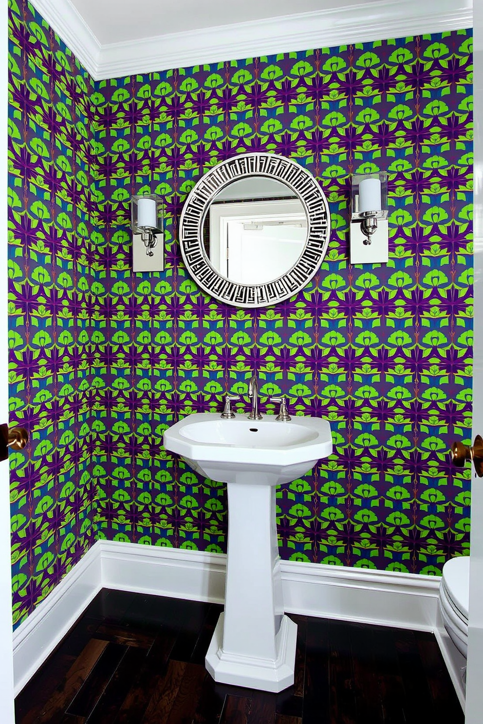 A striking half bathroom featuring bold wallpaper that showcases a vibrant geometric pattern. The wallpaper serves as a statement wall, drawing attention to the sleek white pedestal sink and modern chrome fixtures. The floor is adorned with dark wood tiles that contrast beautifully with the bright wallpaper. A round mirror with a decorative frame hangs above the sink, complemented by stylish lighting fixtures on either side.