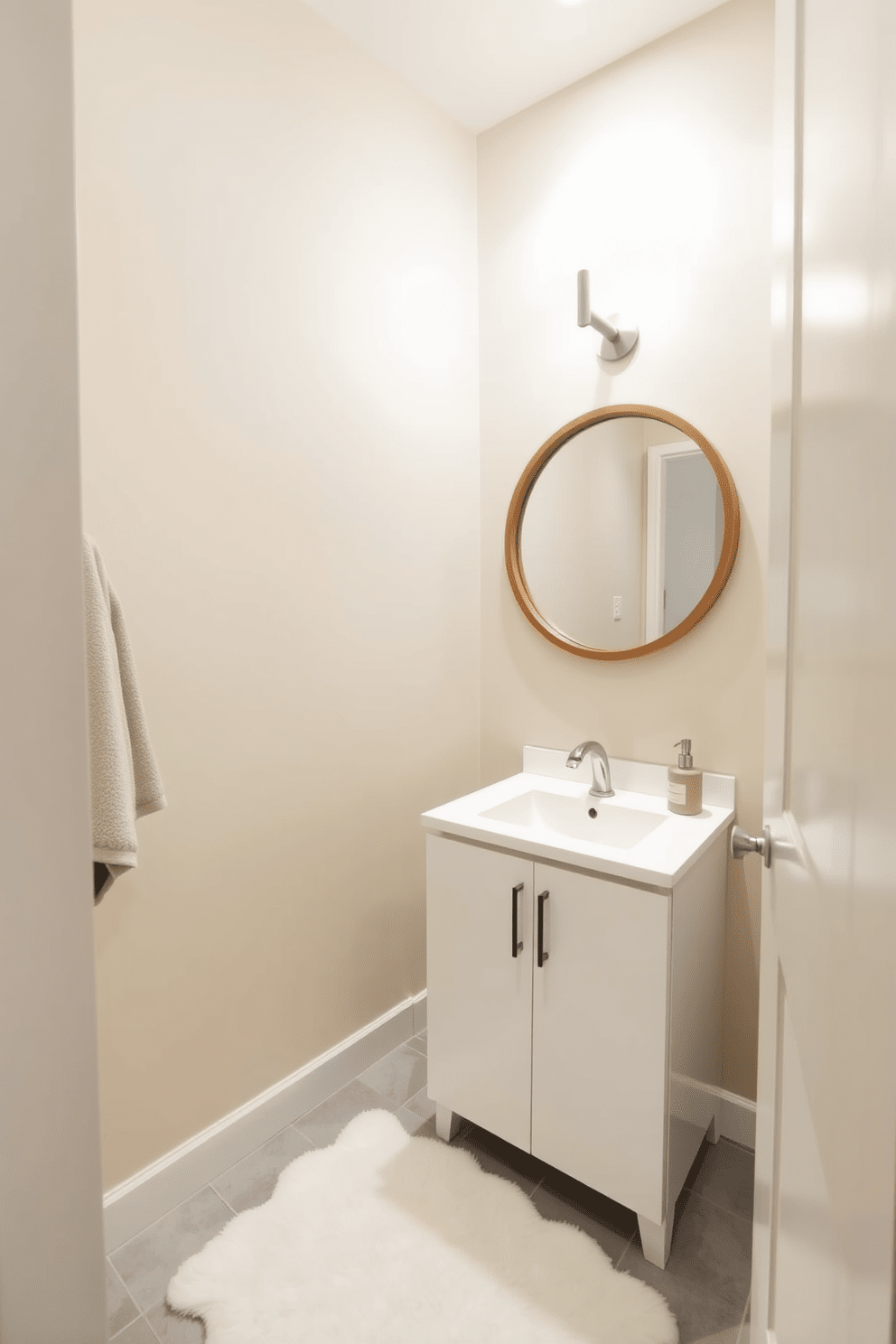 A serene half bathroom featuring neutral tones that create a calming atmosphere. The walls are painted in a soft beige, complemented by a sleek white vanity with a minimalist design. A round mirror with a simple wooden frame hangs above the vanity, reflecting the warm light from a stylish wall sconce. The floor is adorned with light gray tiles, and a plush white rug adds a touch of comfort underfoot.