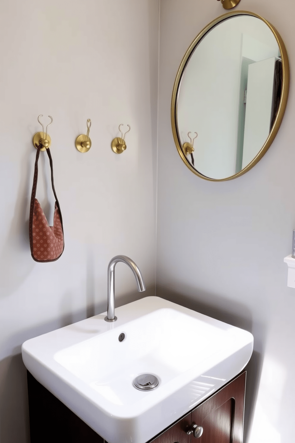 A chic half bathroom featuring decorative hooks on the wall for stylish organization. The hooks are made of brushed brass and are arranged in a visually appealing pattern above a sleek, modern sink with a white ceramic basin. The walls are painted in a soft gray tone, complemented by a dark wood vanity that adds warmth to the space. A round mirror with a minimalist frame hangs above the sink, reflecting natural light from a nearby window.