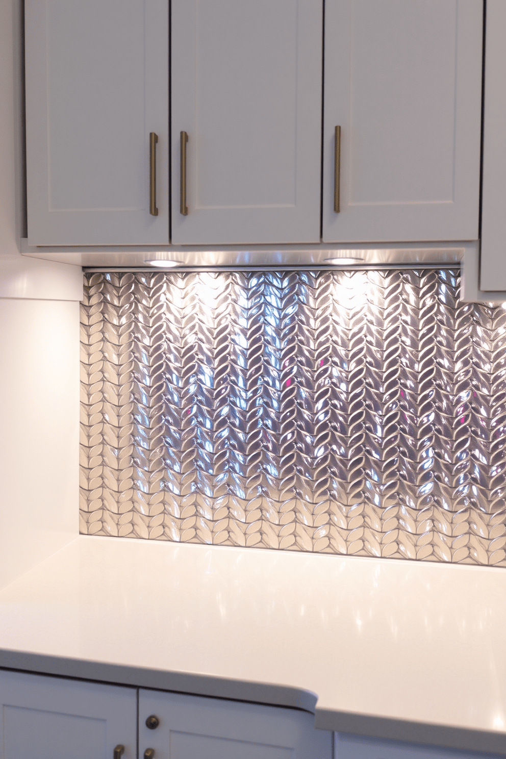 A chic kitchen backsplash featuring shimmering metallic tiles that reflect light beautifully. The tiles are arranged in a herringbone pattern, adding depth and elegance to the space. Complementing the metallic tiles, sleek white cabinetry provides a clean contrast while enhancing the modern aesthetic. Under-cabinet lighting highlights the backsplash, creating a warm and inviting atmosphere in the kitchen.