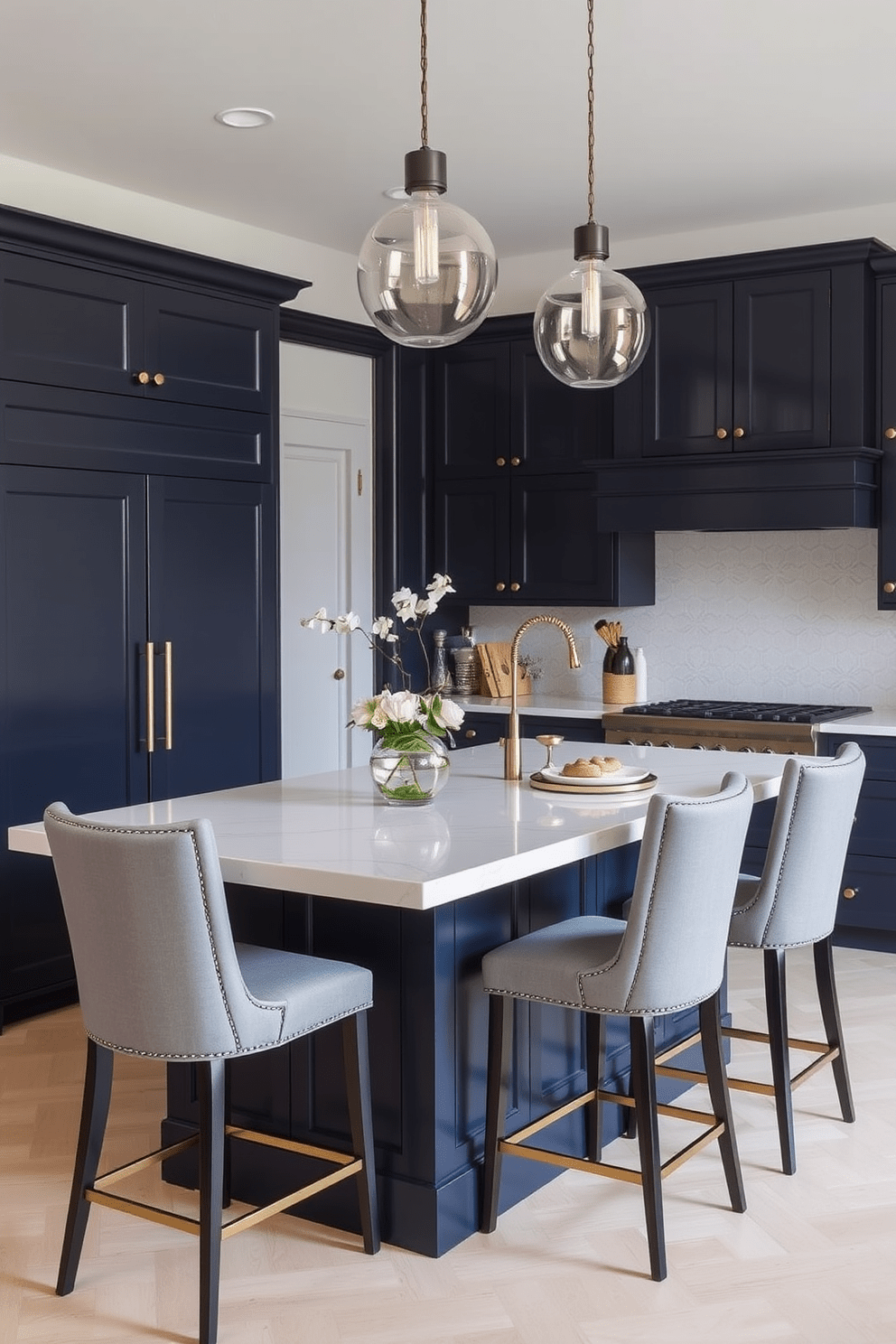 A stylish kitchen island with a sleek quartz countertop serves as the centerpiece of the space. Surrounding the island are high-backed bar stools upholstered in soft gray fabric, creating a comfortable yet elegant dining area. The cabinetry features a rich navy blue finish, complemented by brass hardware that adds a touch of sophistication. Pendant lights with clear glass shades hang above the island, illuminating the space with a warm glow.