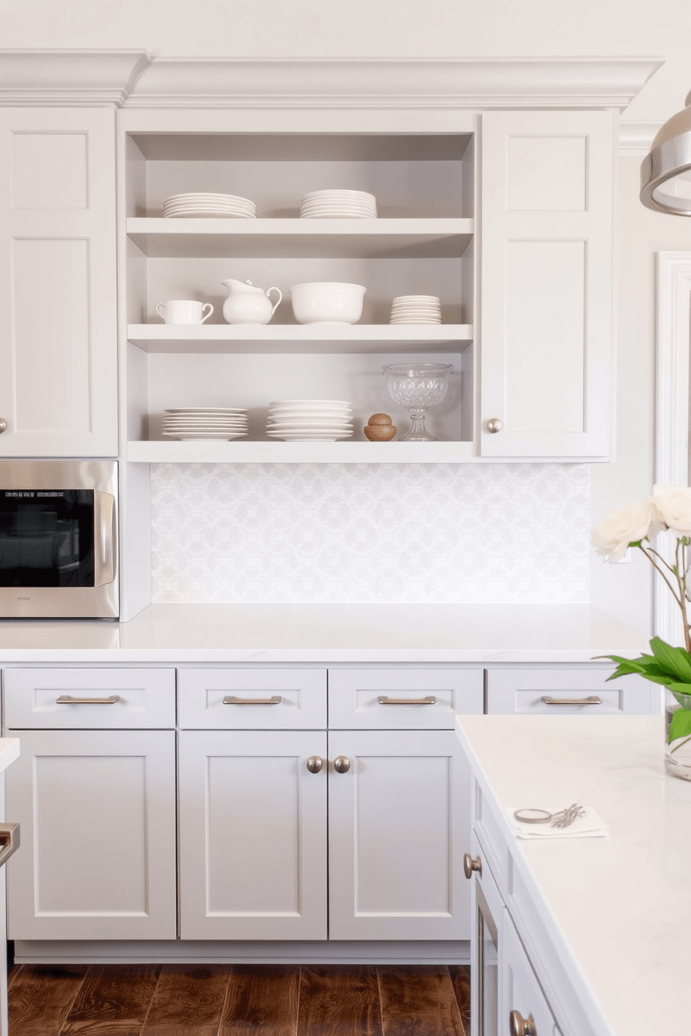 A soft and inviting kitchen features light gray cabinets that create a serene atmosphere. The cabinets are complemented by brushed nickel handles and a white quartz countertop that enhances the overall brightness of the space. Above the cabinets, open shelving displays carefully curated dishware and decorative items. A stylish backsplash in a subtle pattern ties the design together, adding texture and interest to the kitchen.