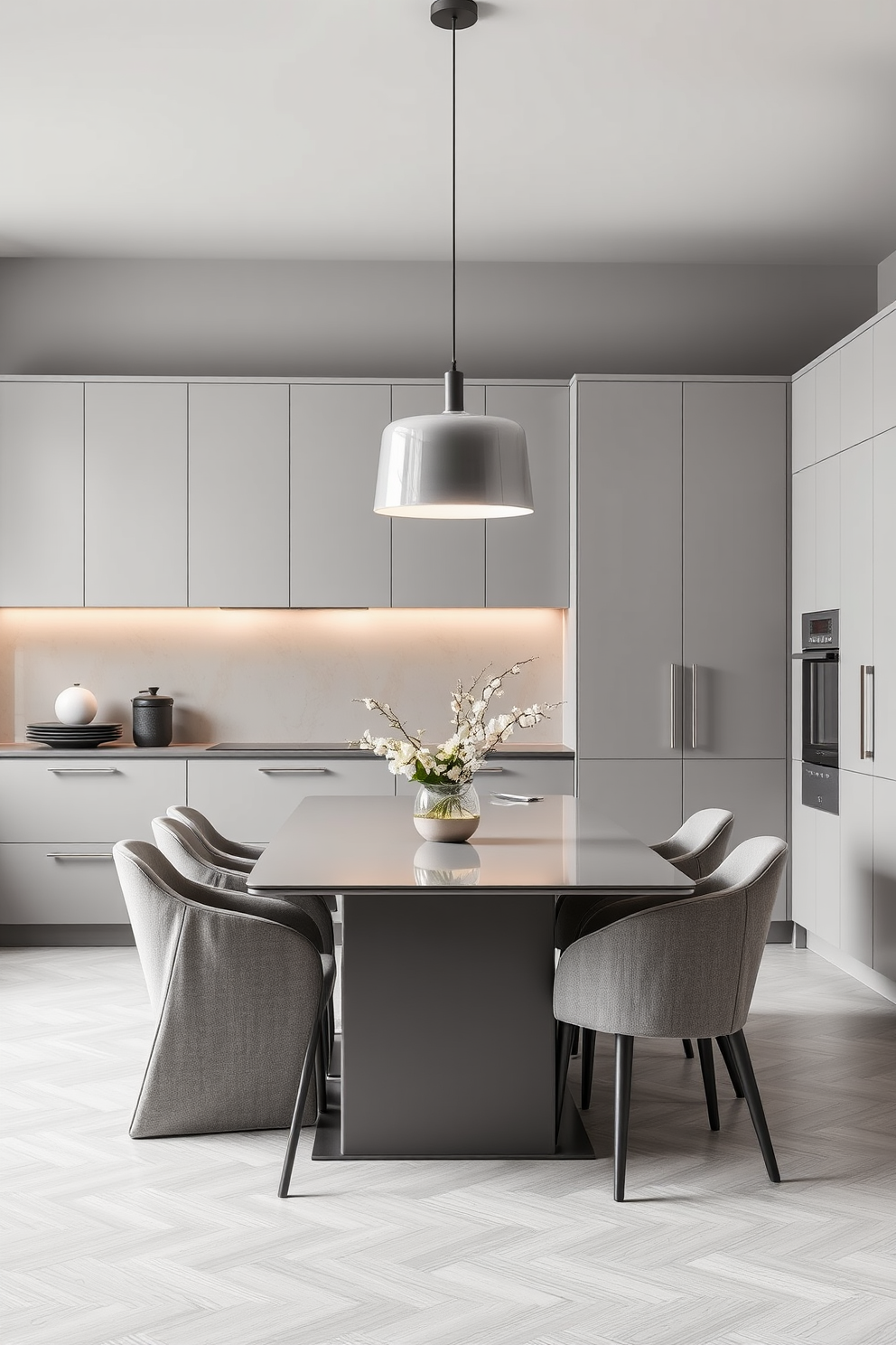 A sleek kitchen dining room with a monochromatic color scheme showcasing shades of gray. The dining table is a modern rectangular design with matching upholstered chairs, creating a sophisticated atmosphere. The cabinetry features minimalist handles and a seamless finish, enhancing the elegant look. A statement pendant light hangs above the table, casting a warm glow over the space.