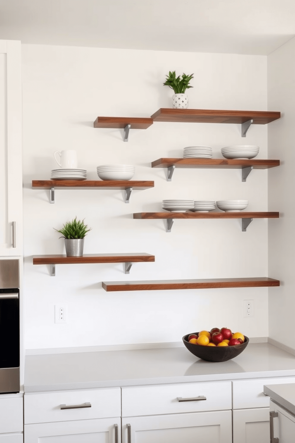 A modern kitchen featuring sleek wall-mounted shelves made of reclaimed wood. The shelves are arranged in a staggered pattern, displaying stylish dishware and decorative plants for a touch of greenery. The cabinetry is painted in a soft white, complemented by brushed nickel hardware. Below the shelves, a spacious countertop provides ample workspace, with a bowl of fresh fruits adding a pop of color.