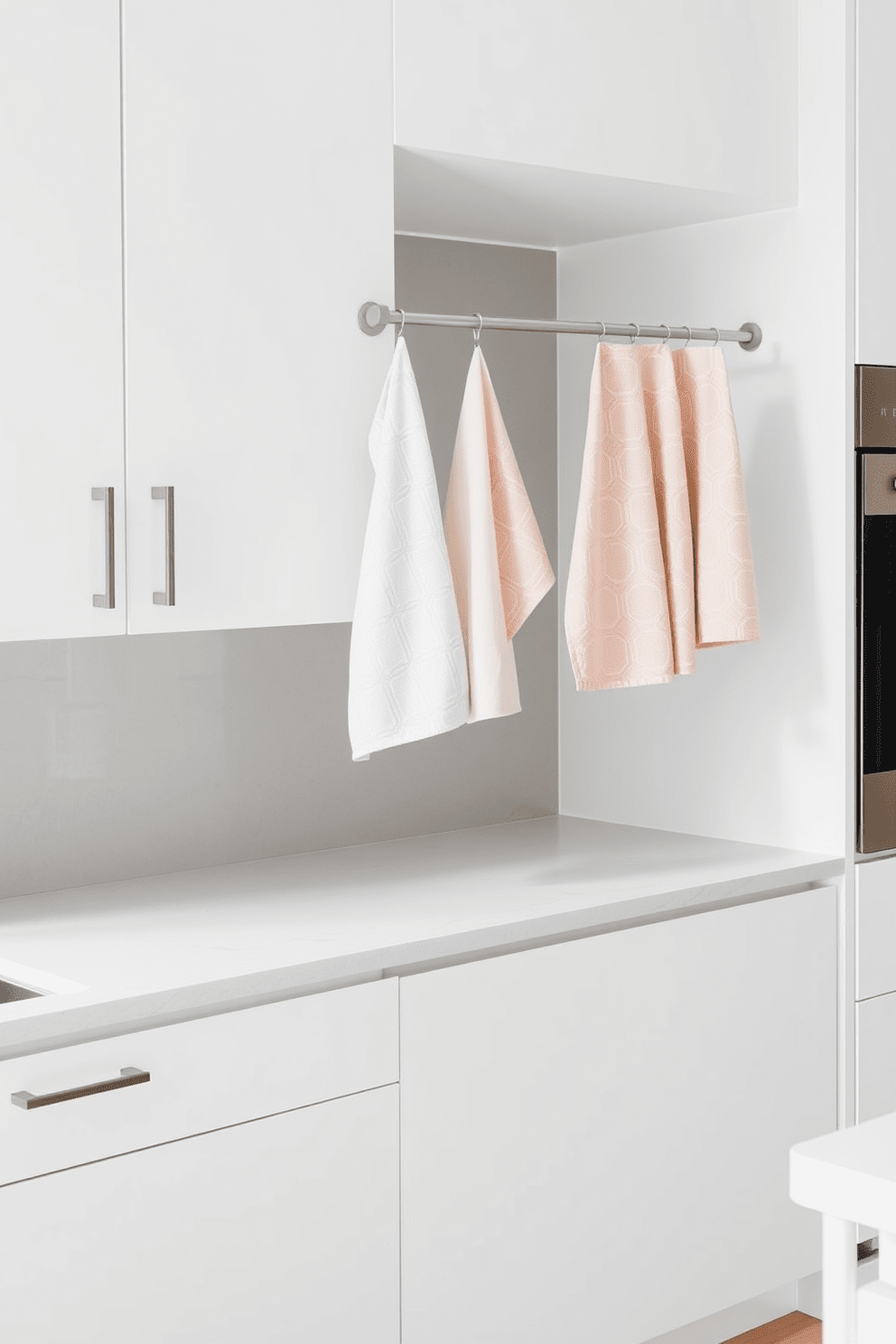 A minimalist kitchen featuring sleek cabinetry in a soft white finish. The countertops are made of polished quartz, and a simple backsplash in muted gray complements the overall aesthetic. A set of elegant kitchen towels in subtle pastel colors hangs neatly on a modern rack. Each towel showcases a delicate geometric pattern that enhances the clean and organized look of the space.