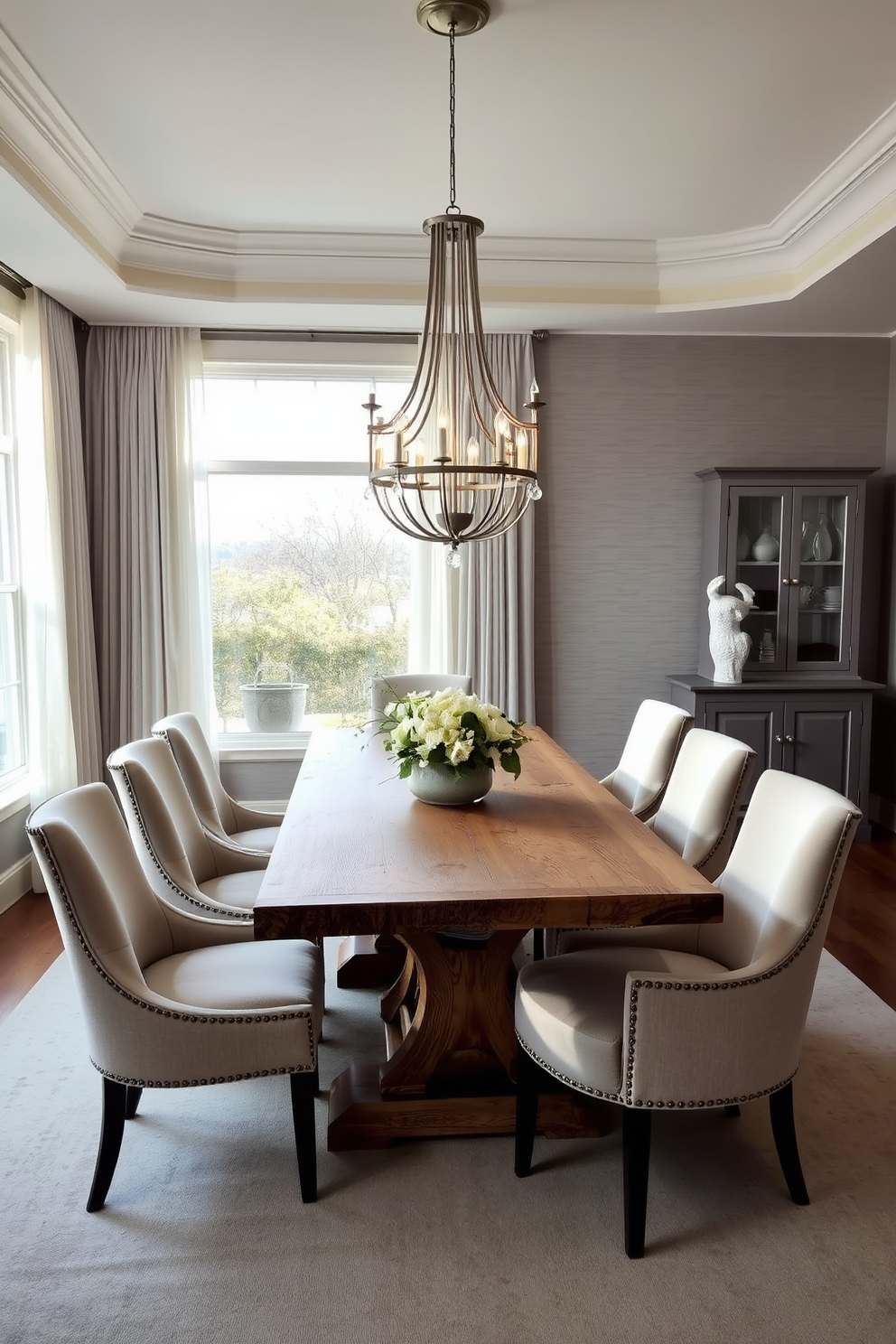 An elegant L-shaped dining room featuring a cohesive color palette of soft greys and warm whites. The dining table is made of reclaimed wood, surrounded by plush upholstered chairs in a complementary fabric. A statement chandelier hangs above the table, casting a warm glow over the space. The walls are adorned with subtle textured wallpaper, enhancing the room's sophistication. Large windows allow natural light to flood in, framed by sheer curtains that add a touch of softness. A sideboard in a matching finish provides additional storage and display space for decorative items.