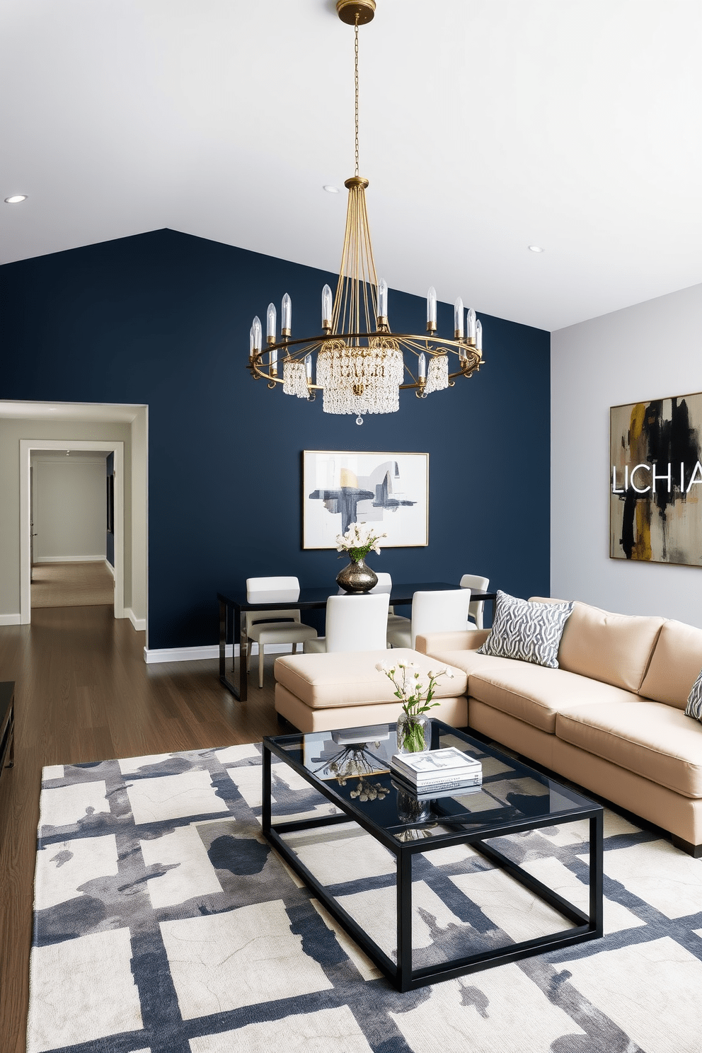 A spacious living room featuring a deep navy blue accent wall paired with a light beige sectional sofa. A large area rug with bold geometric patterns anchors the seating area, while a glass coffee table adds a modern touch. In the dining area, a sleek black dining table is surrounded by white upholstered chairs. Above the table, a striking chandelier with gold accents creates a focal point, complemented by a large abstract artwork on the adjacent wall.