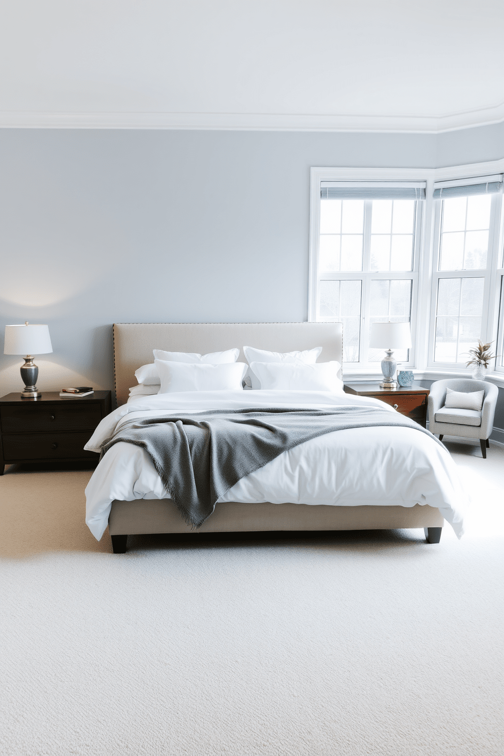 A serene large bedroom with a plush king-sized bed dressed in soft white linens and layered with a light gray throw blanket. Flanking the bed are two elegant nightstands made of dark wood, each topped with stylish lamps that emit a warm glow. The walls are painted in a soothing pastel blue, creating a tranquil atmosphere. A cozy reading nook is positioned by a large window, featuring a comfortable armchair and a small side table adorned with a stack of books and a decorative plant.