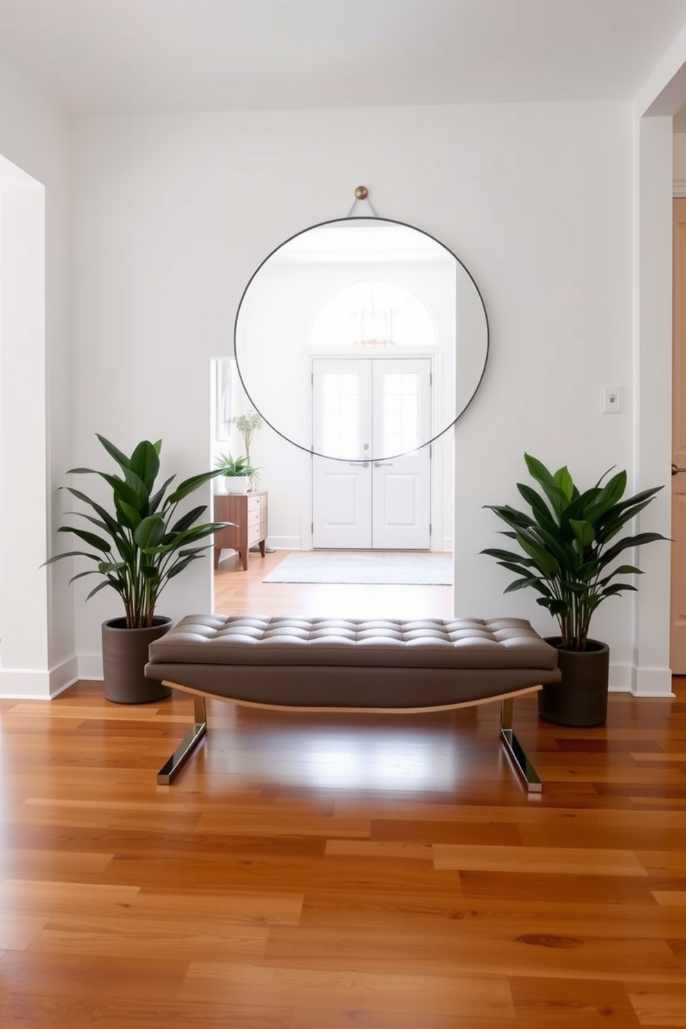 A modern bench with sleek lines is positioned against a backdrop of a spacious entryway. The walls are adorned with minimalist artwork, and a large round mirror reflects natural light, enhancing the open feel of the space. The floor features polished hardwood, creating a warm contrast with the contemporary bench. Potted plants flank the entrance, adding a touch of greenery and inviting atmosphere.