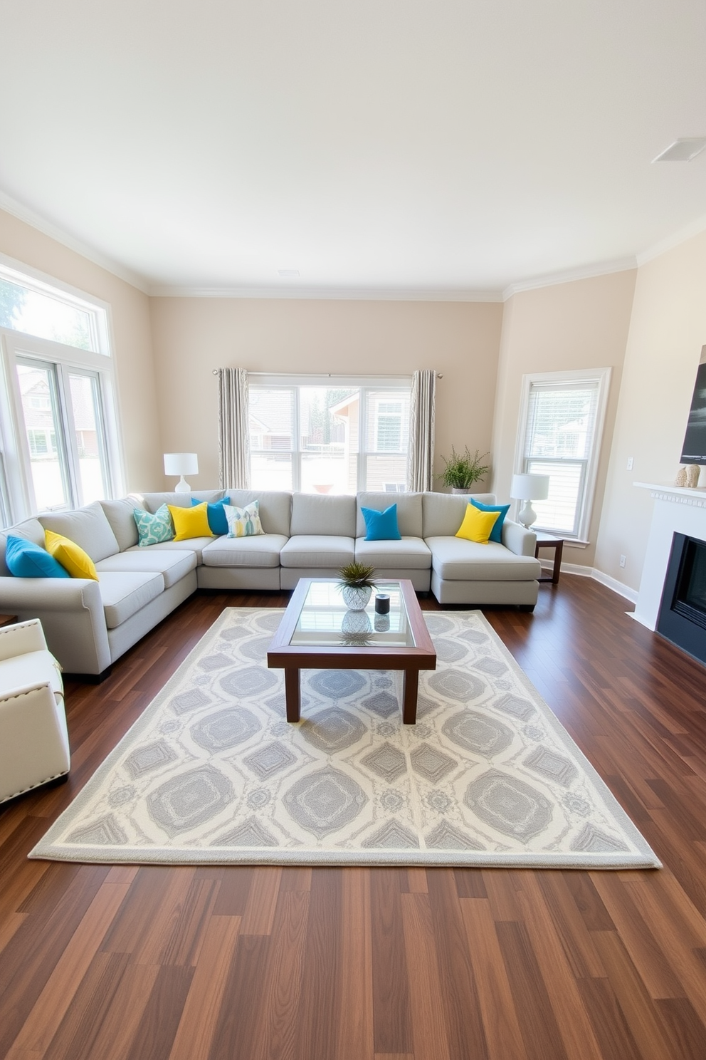 A spacious family room featuring a neutral color palette with soft beige walls and a light gray sectional sofa. Colorful accent pillows in vibrant hues of blue and yellow are scattered across the sofa, adding a playful touch to the design. In the center, a large area rug with geometric patterns anchors the seating area, while a wooden coffee table with a glass top provides a functional centerpiece. Floor-to-ceiling windows allow natural light to flood the room, creating a warm and inviting atmosphere.