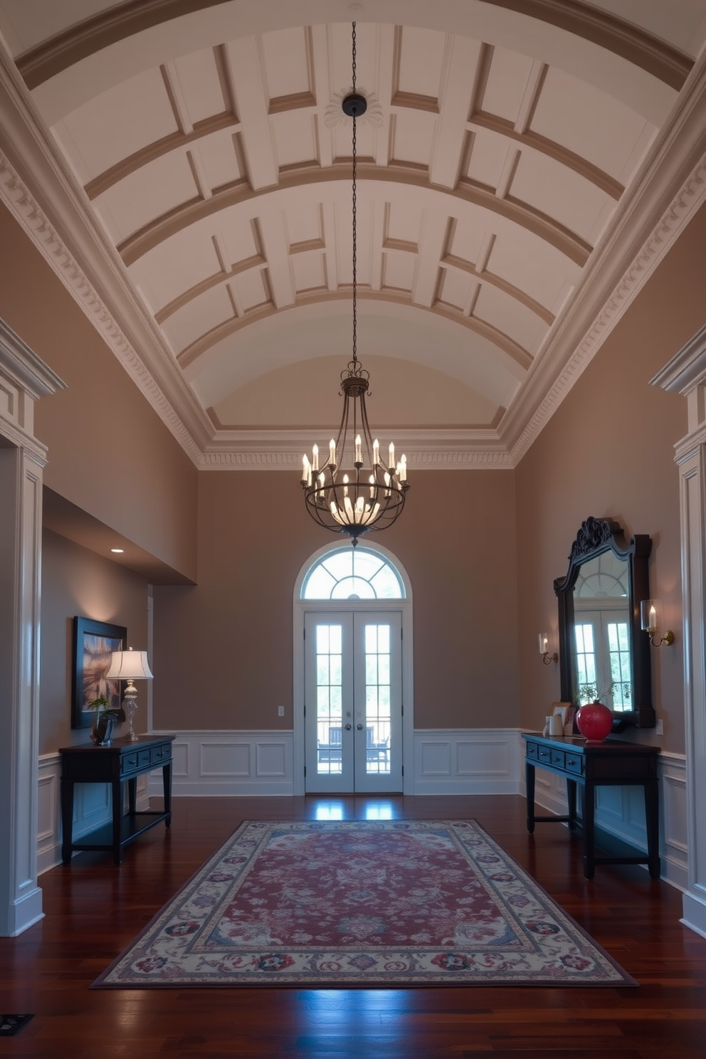 A grand foyer featuring a high vaulted ceiling with intricate crown molding. The space is illuminated by an elegant chandelier that hangs gracefully in the center, casting a warm glow. Rich hardwood flooring complements the classic design, while a large area rug adds texture and warmth. A statement console table against the wall displays decorative art pieces and a large mirror that enhances the sense of space.