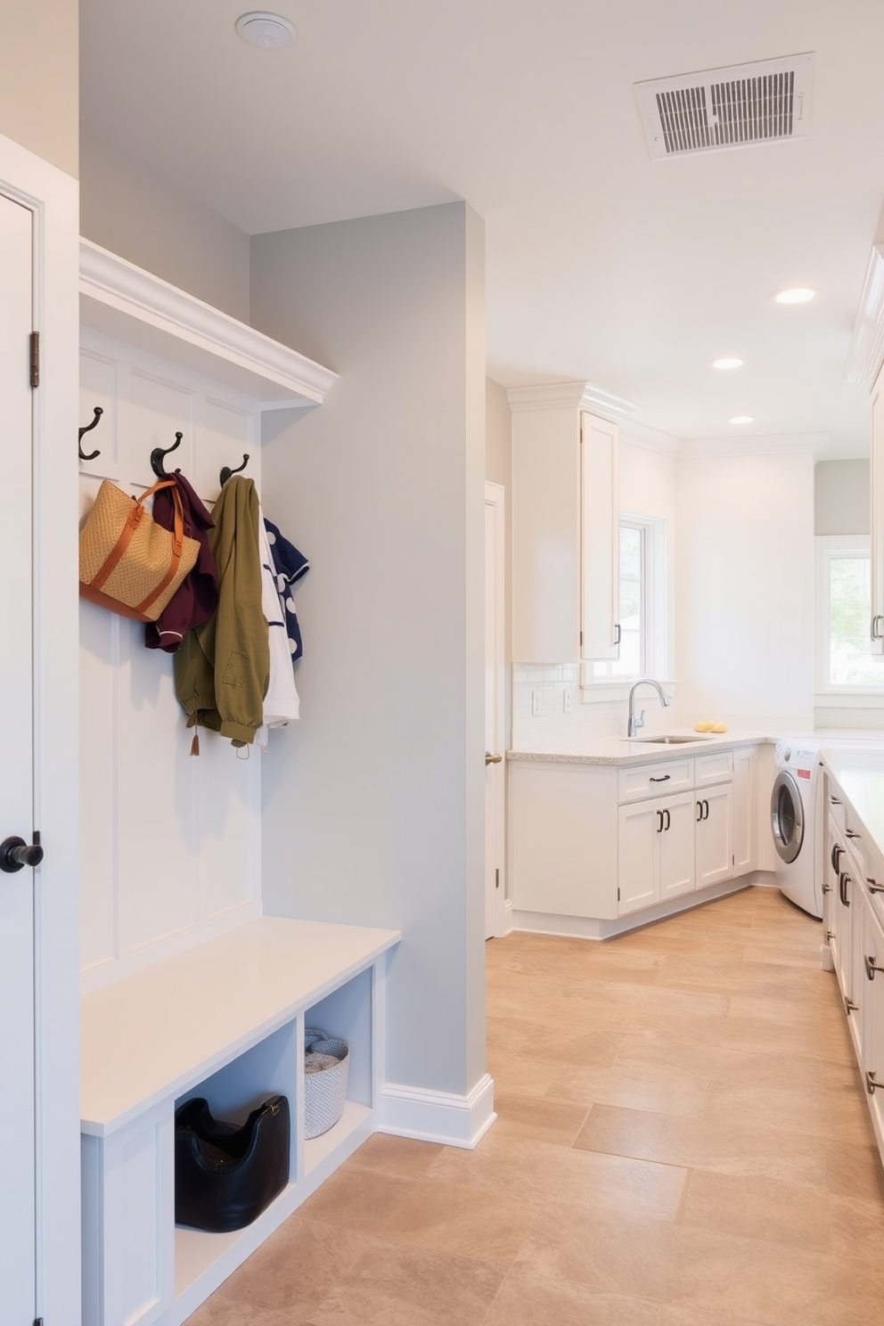 A functional mudroom adjacent to the laundry room features built-in storage benches with hooks above for coats and bags. The walls are painted a soft gray, and the floor is covered in durable ceramic tiles for easy cleaning. The large laundry room includes expansive countertops for folding clothes and a double sink for hand-washing. Bright white cabinetry lines the walls, providing ample storage, while a window allows natural light to fill the space.