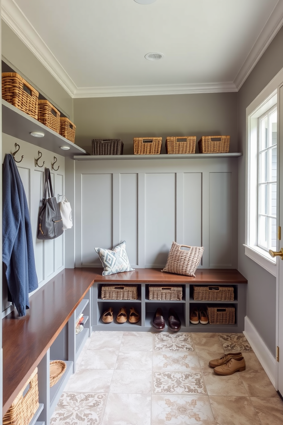 A spacious mudroom features a combination of built-in benches and hooks for coats. Decorative baskets are neatly arranged on shelves, providing stylish storage options for shoes and outdoor gear. The walls are painted in a soft gray hue, complemented by a durable tile floor. A large window allows natural light to flood the space, enhancing the inviting atmosphere.