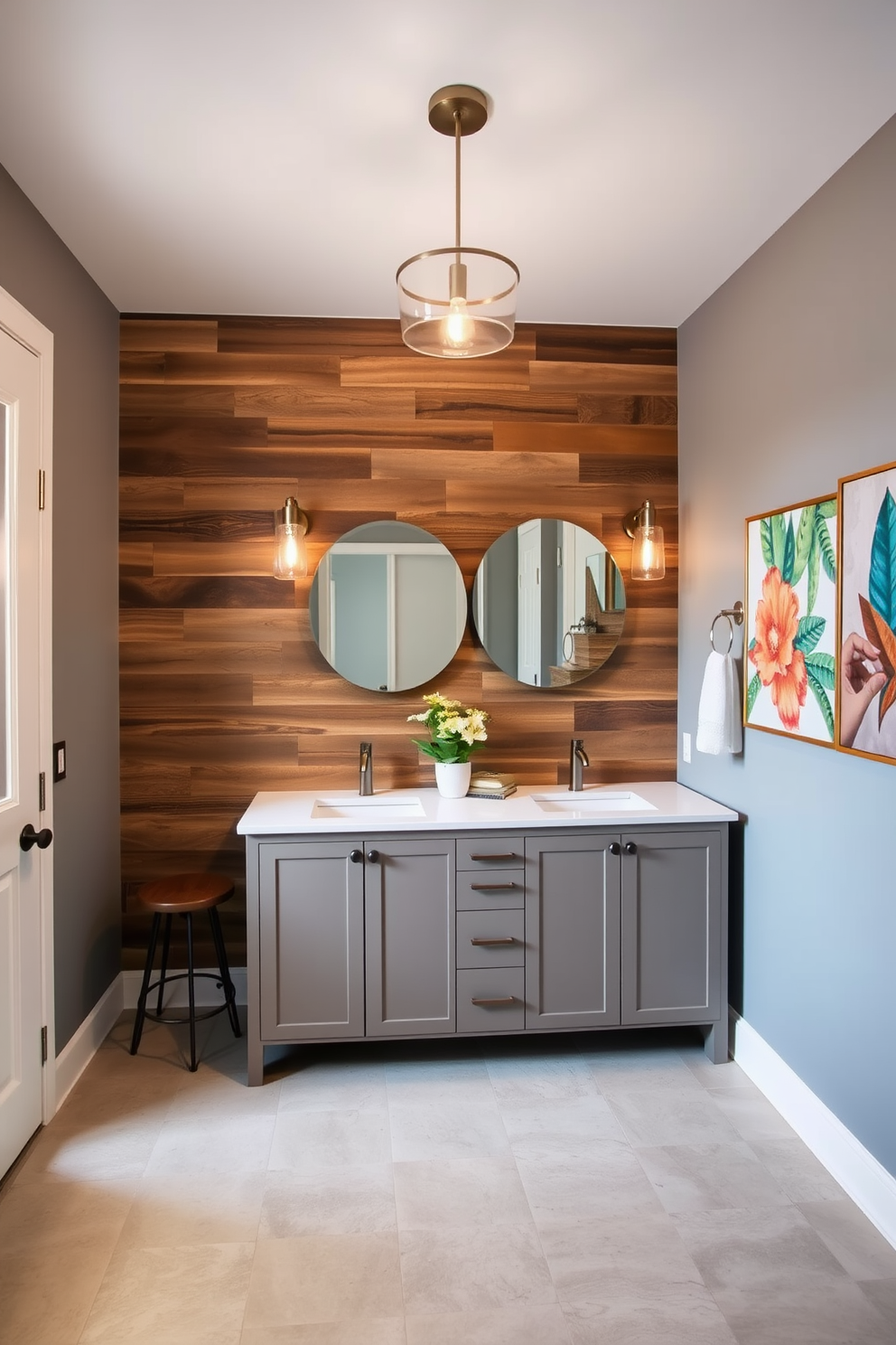 A stunning powder room featuring an accent wall made of reclaimed wood that adds warmth and texture. The other walls are painted in a soft gray, creating a sophisticated backdrop for the space. A large freestanding vanity with double sinks is positioned against the wood accent wall, topped with a luxurious quartz countertop. Elegant pendant lights hang above the vanity, illuminating the space with a warm glow. The flooring consists of large format porcelain tiles in a neutral tone, offering a sleek and modern look. A stylish round mirror above the vanity reflects the beautiful design elements, enhancing the room's spacious feel. Decorative elements such as a chic stool and a vibrant piece of artwork complete the room, adding personality and flair. Fresh greenery in a decorative pot brings life to the space, making it both inviting and stylish.