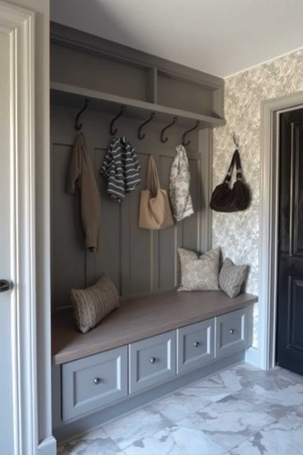 A stylish mudroom featuring a built-in bench with plush cushions. Above the bench, there are several hooks for hanging coats and bags, creating an organized and inviting space. The walls are painted in a soft gray hue, complemented by a patterned wallpaper on one side. The floor is covered with durable, easy-to-clean tiles that add a touch of elegance to the functional area.