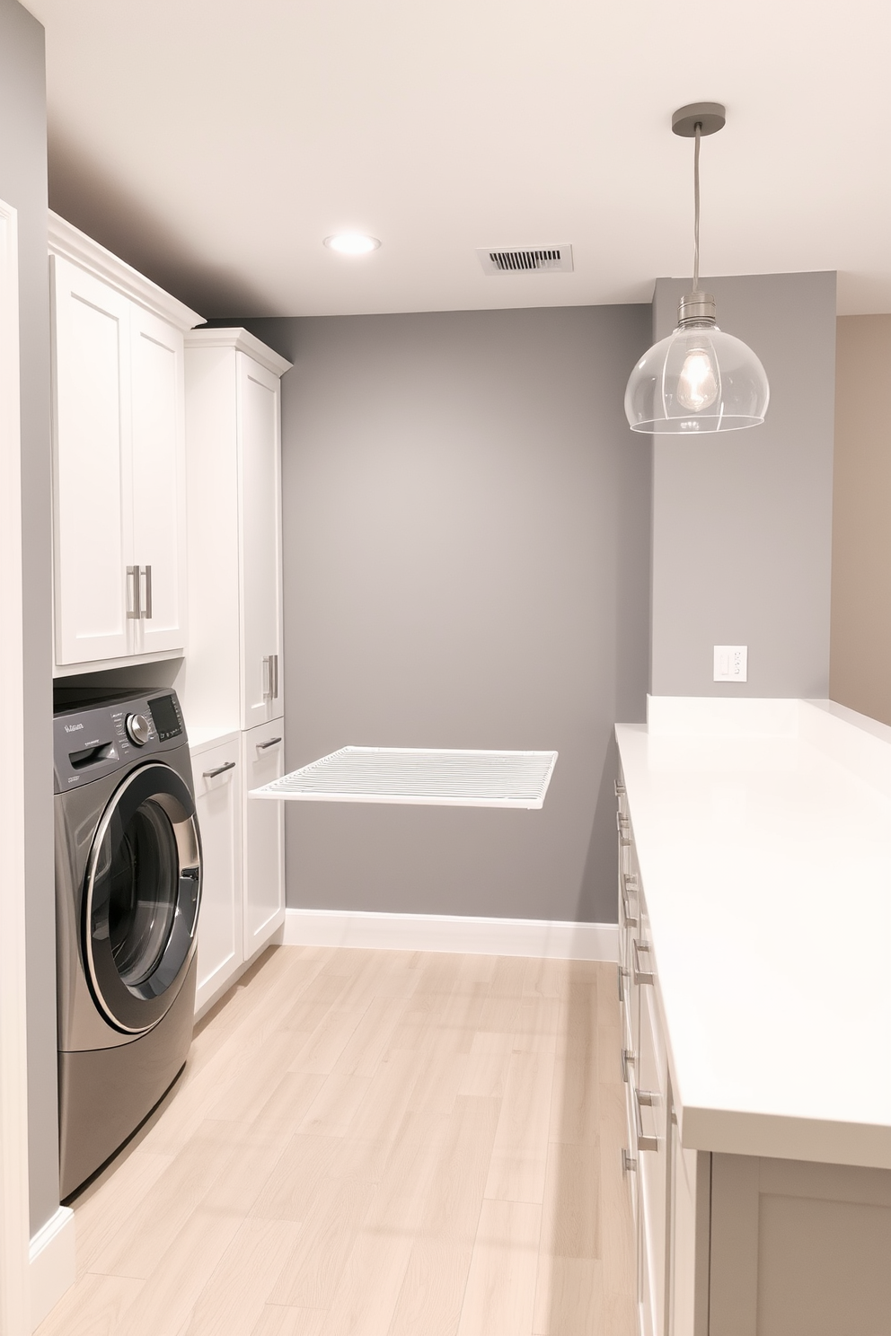 A modern laundry room in a basement setting featuring a sleek drying rack designed for delicate items. The walls are painted in a soft gray tone, and the floor is covered with durable vinyl planks in a light wood finish. To the left of the drying rack, there are built-in cabinets for storage, painted in a crisp white. A large countertop for folding clothes runs along the opposite wall, complemented by a stylish pendant light hanging above.