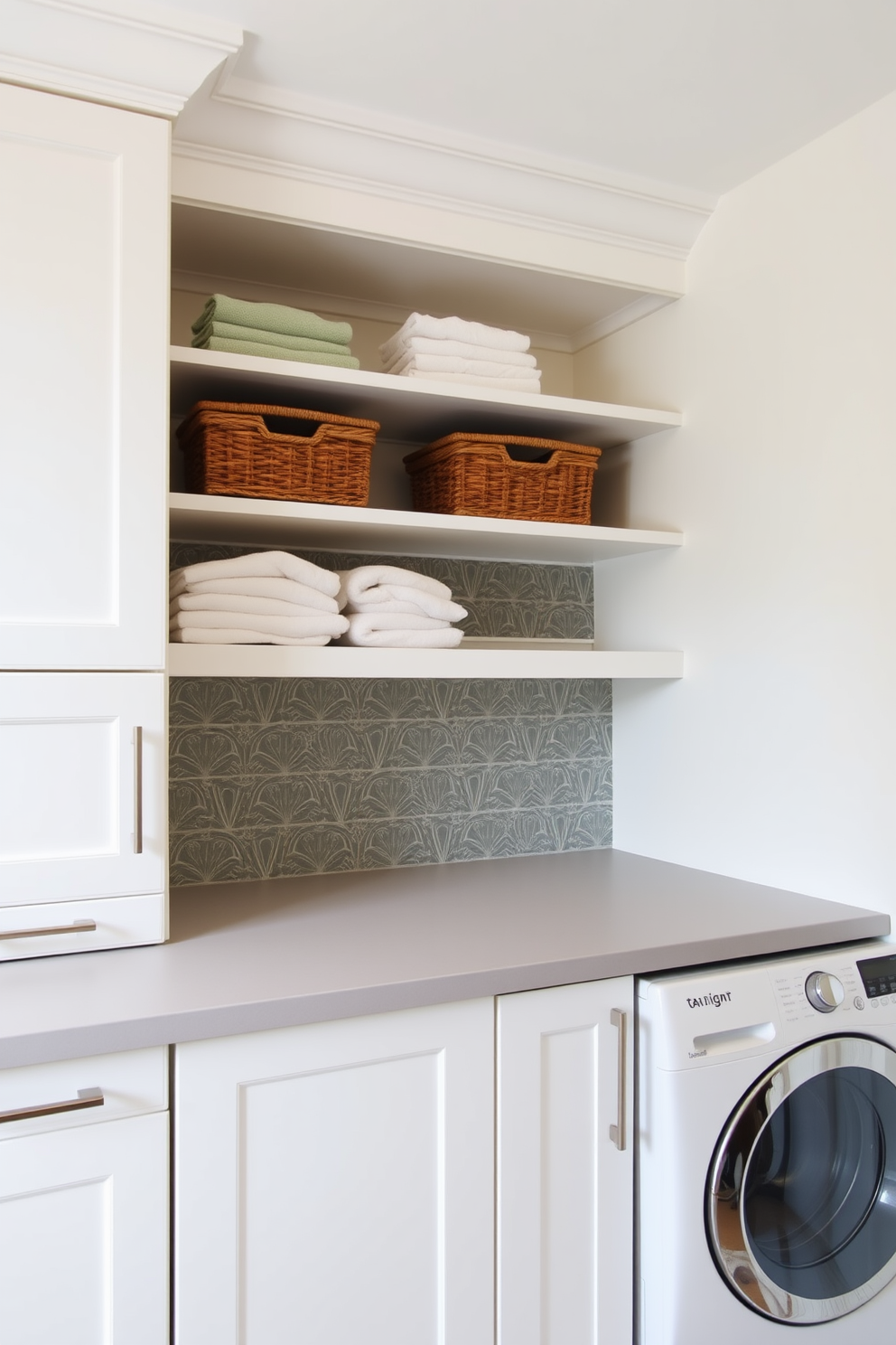 Stylish cabinetry designed for a laundry room features sleek white doors with brushed nickel handles. The cabinetry is complemented by a light gray countertop, providing ample workspace for folding clothes. Above the countertop, open shelving showcases neatly stacked towels and decorative storage baskets. The walls are painted in a soft pastel hue, and a stylish backsplash adds a pop of color to the space.