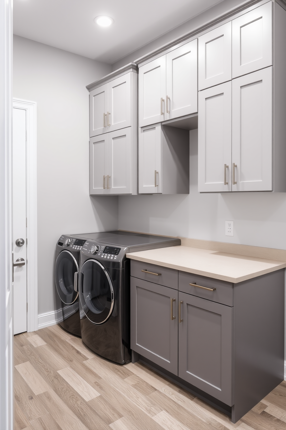 A modern laundry room that doubles as a utility space. The room features a sleek countertop for folding clothes, with built-in storage cabinets above and below for organization. On one side, a stacked washer and dryer are seamlessly integrated into the cabinetry. The walls are painted in a light gray hue, and the floor is covered with durable vinyl planks that mimic wood.