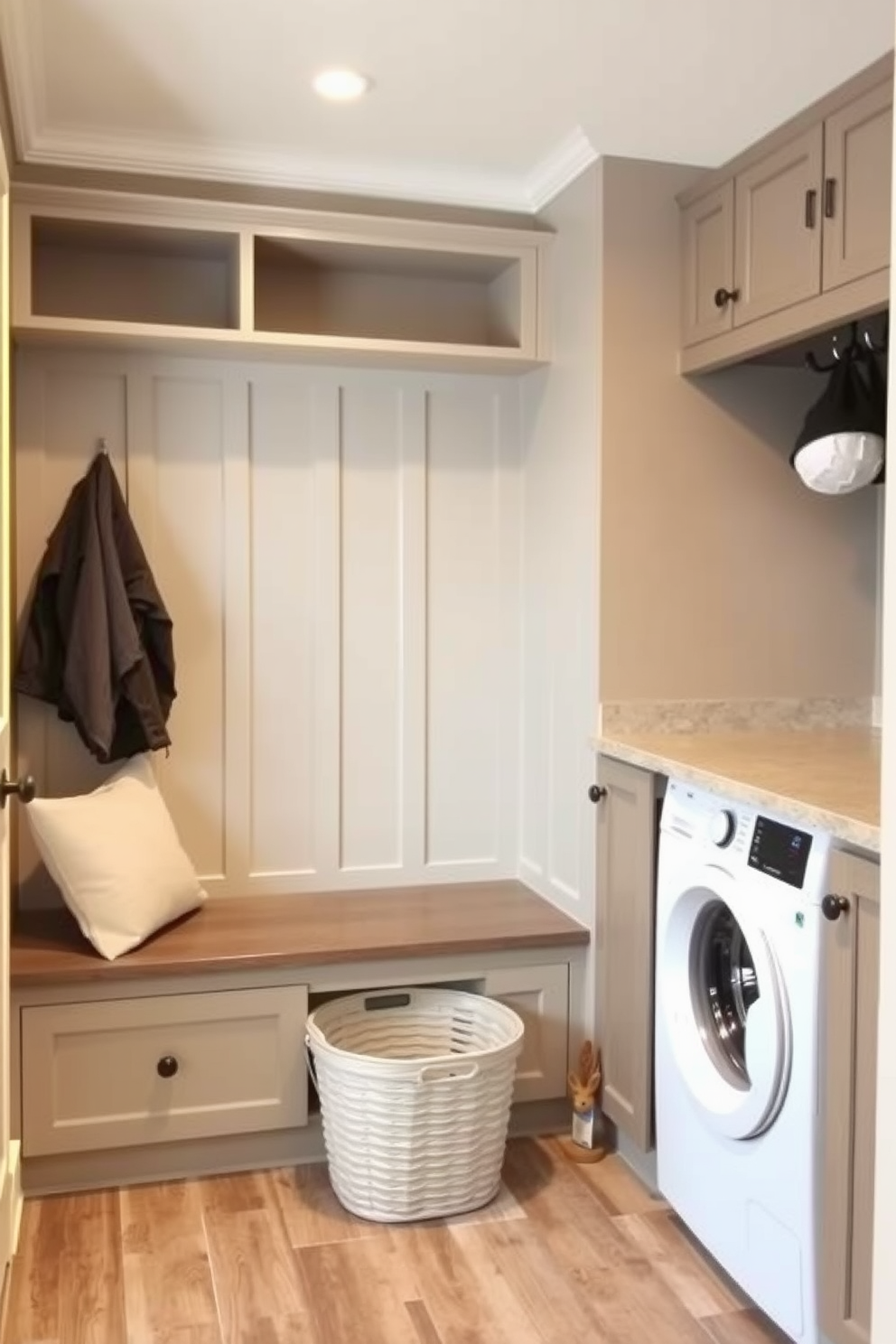 A functional mudroom laundry combo space featuring a built-in bench with storage cubbies above. The walls are painted in a soft gray, and the floor is covered with durable tile that mimics wood. To the right, a stacked washer and dryer are neatly tucked into cabinetry with a countertop for folding clothes. A large basket for dirty laundry sits beside the bench, and hooks for coats and bags are mounted on the wall above.