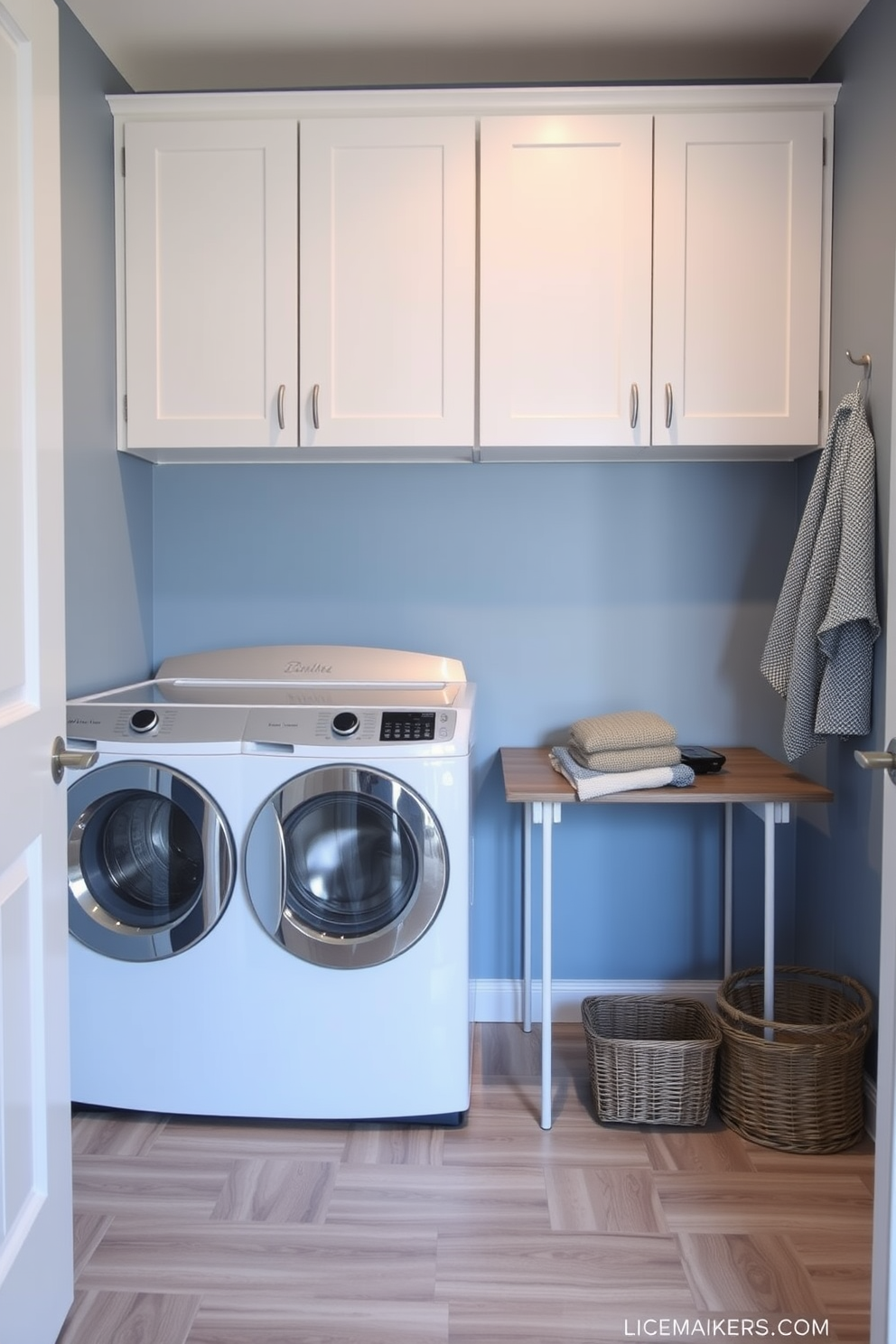 A modern laundry room featuring a top loading washer positioned next to a sleek folding table for added convenience. The walls are painted in a soft blue hue, complemented by white cabinetry above for storage and organization. The floor is adorned with durable vinyl tiles that mimic the look of wood, providing both style and functionality. A wicker basket sits beside the folding table, ready to hold freshly laundered clothes.