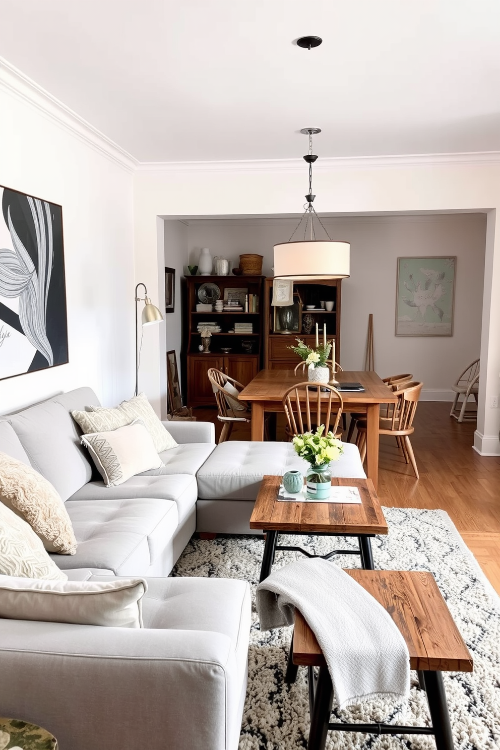 A living room and dining room combo featuring a cozy sectional sofa upholstered in soft gray fabric. The dining area showcases a rustic wooden table surrounded by mismatched chairs, adding character to the space. Layered textiles create warmth and visual interest, with a plush area rug anchoring the seating area. A statement pendant light hangs above the dining table, illuminating the space with a warm glow.