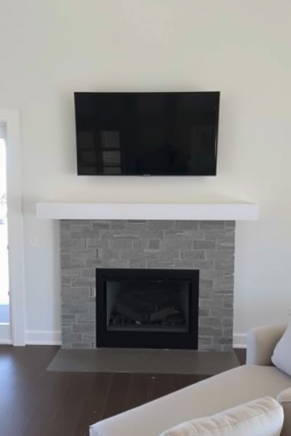 A modern living room features a sleek mantel beneath a flat-screen TV, creating a focal point that blends functionality with style. The fireplace, framed in minimalist stone, adds warmth and elegance, while a plush sectional sofa invites comfort and relaxation.